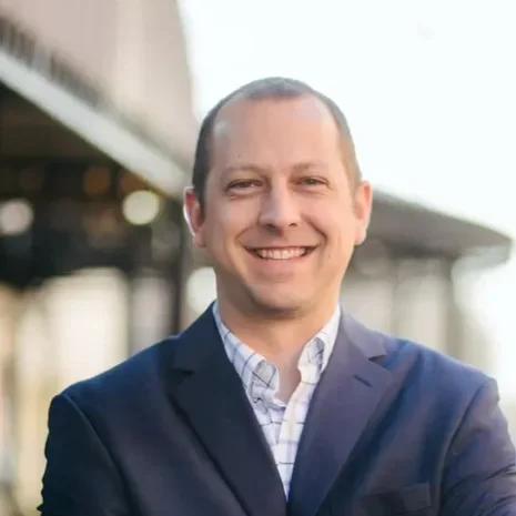 Portrait of a man in a suit smiling outdoors in front of a building