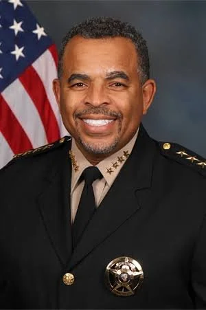 Portrait of a man in a police uniform with an American flag in the background.