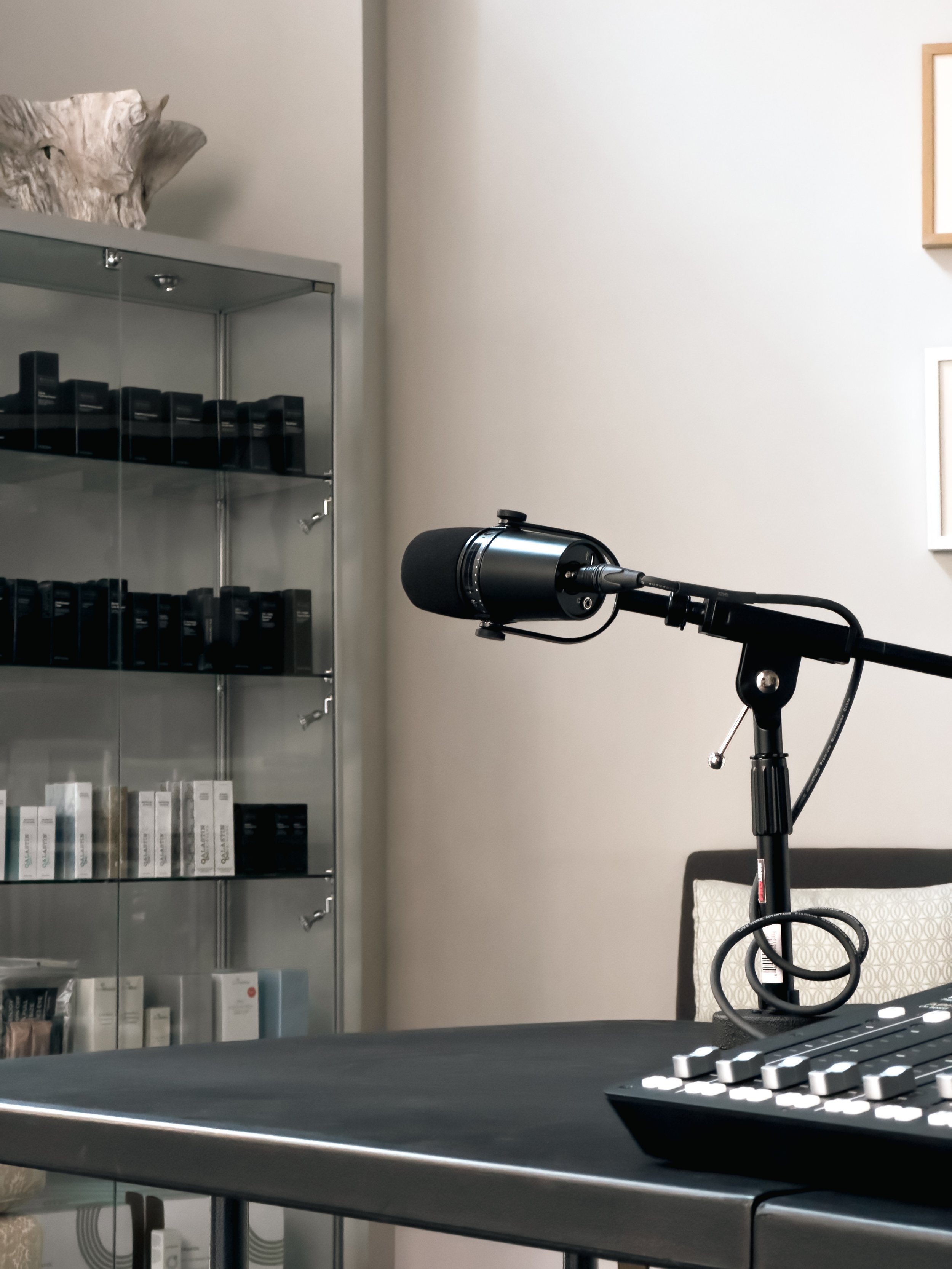 A microphone on a stand, a computer keyboard, a glass display cabinet with various boxes inside, and a decorative wooden bowl on top of the cabinet in a room with white walls.