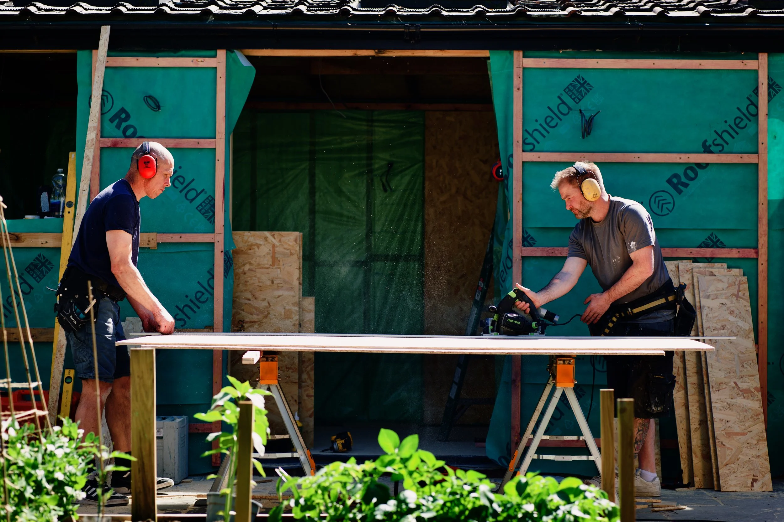 Builders cutting timber on site during garden room construction, with breathable membrane wall wrap visible