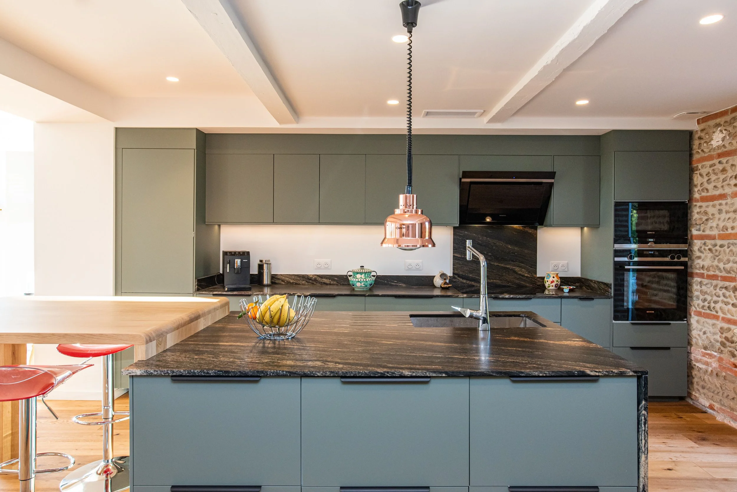 Kitchen extension in Bristol with sage green cabinetry, dark granite worktops, and an exposed brick feature wall