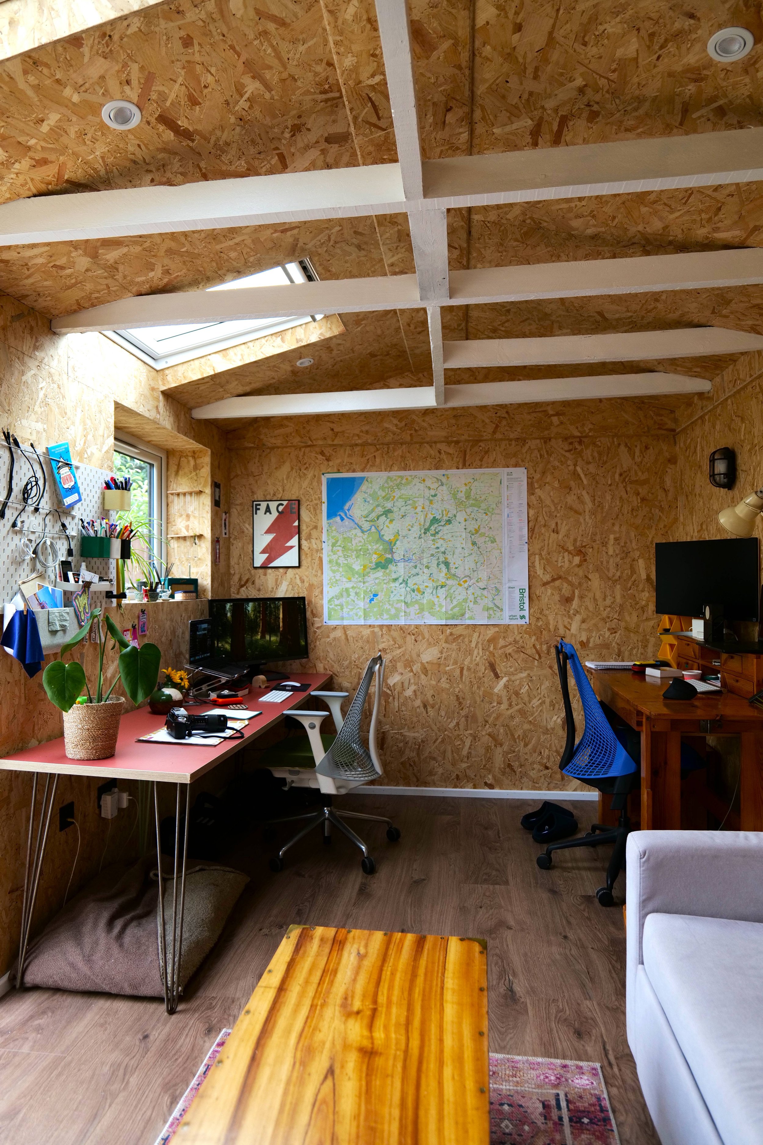 Garden office interior with OSB board walls, exposed painted beams, and skylights, fitted with two desks and ergonomic chairs
