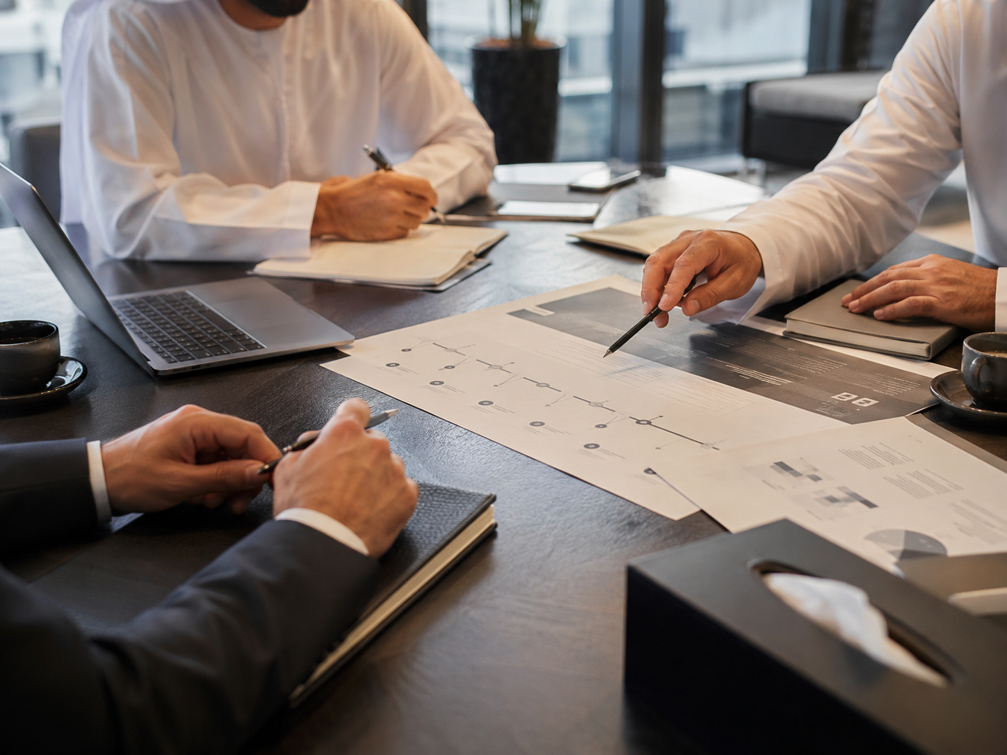 Business professionals in a meeting discussing documents and charts, with laptops and coffee cups on the table.