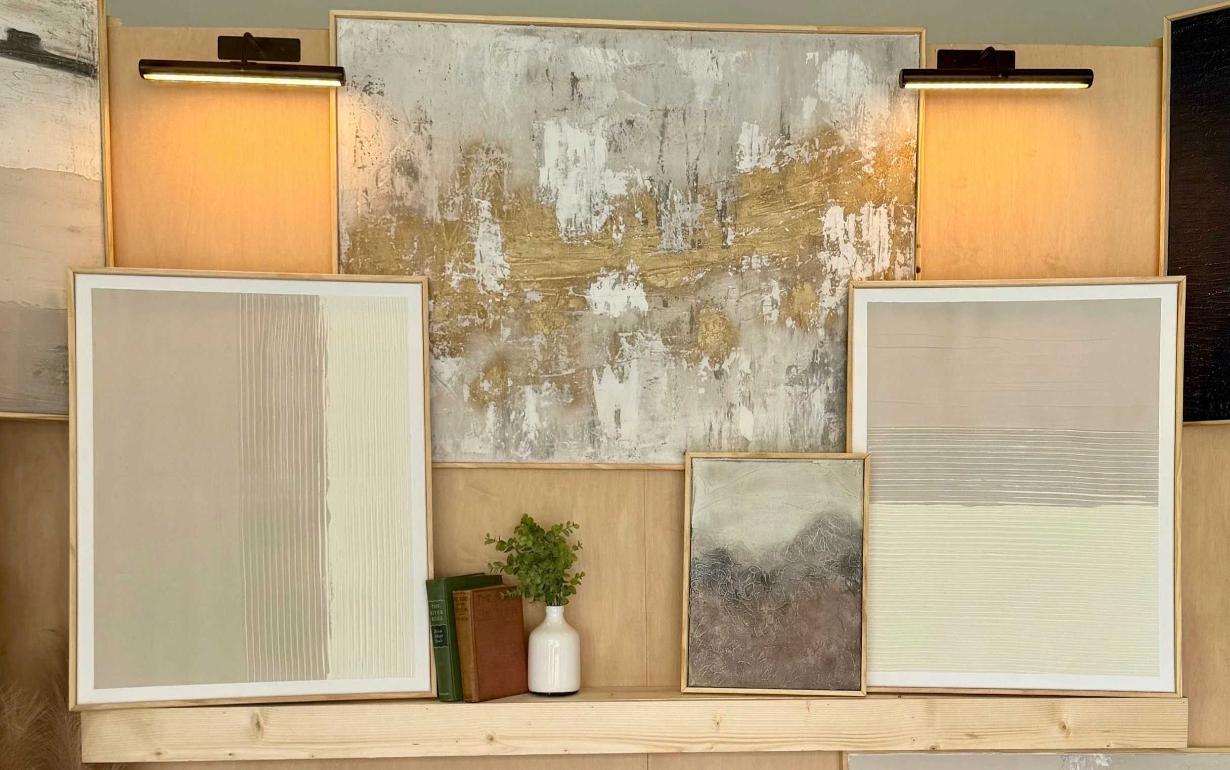 Display of various textured wall and tile samples arranged vertically on a wall, with a small plant and books placed on a shelf at the bottom.