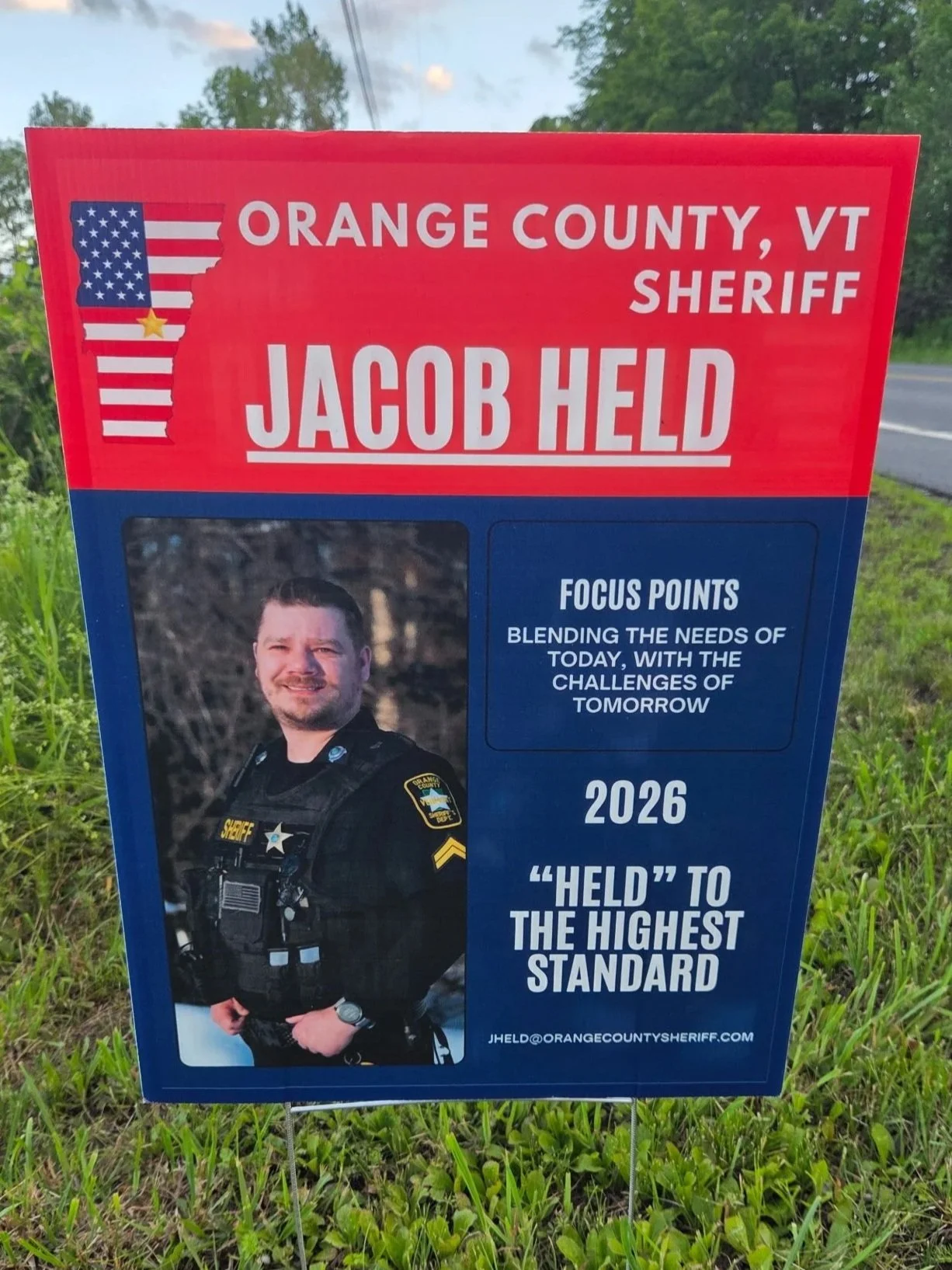 Campaign sign for Jacob Held, running for sheriff in Orange County, Vermont, featuring his portrait in a sheriff's uniform and campaign messages emphasizing service and standards.