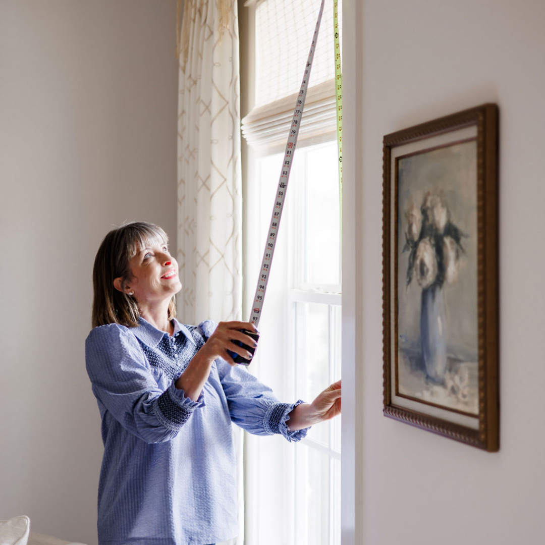 A woman measuring the window height with a tape measure inside a house.