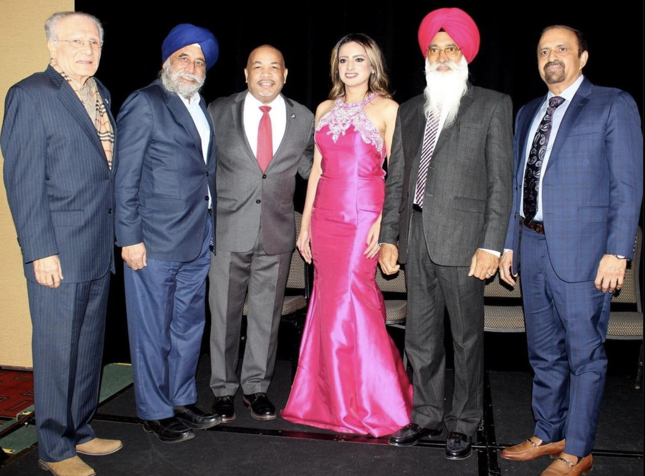 Group of seven people dressed in formal attire, standing together and smiling for the photo, with a woman in a bright pink gown in the center.