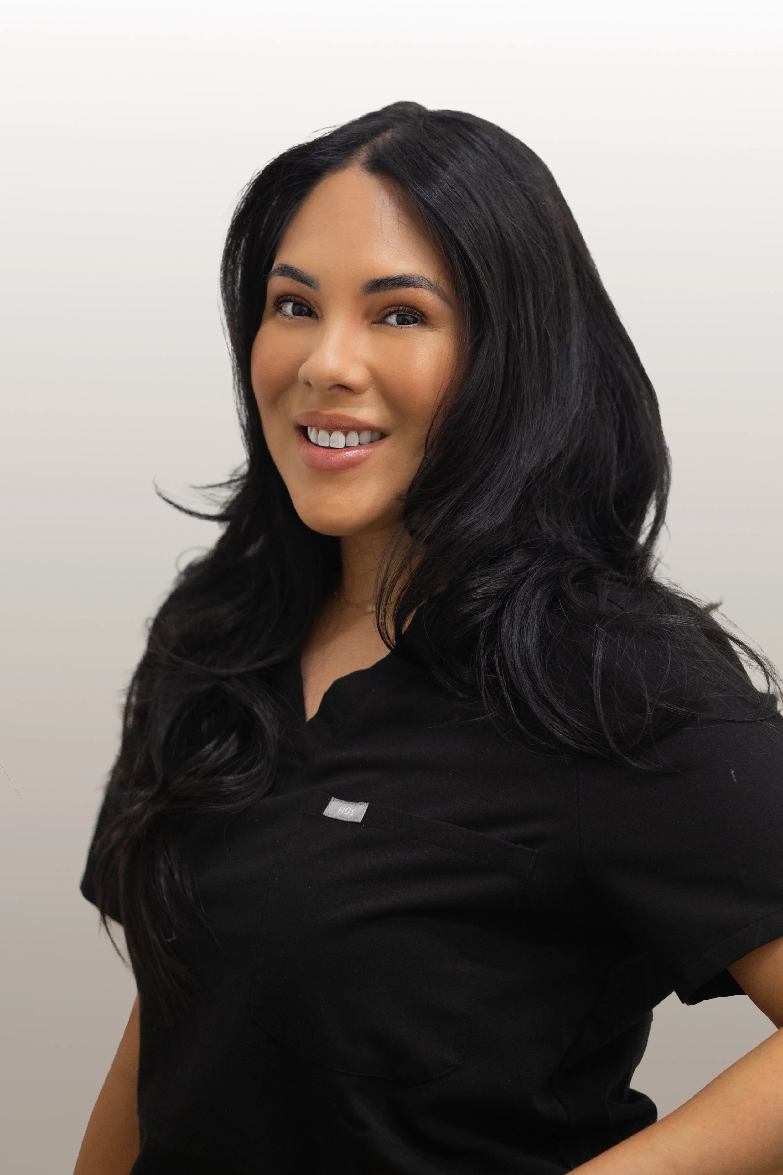 Close-up of a woman with long black hair smiling, wearing a black shirt, against a plain white background.
