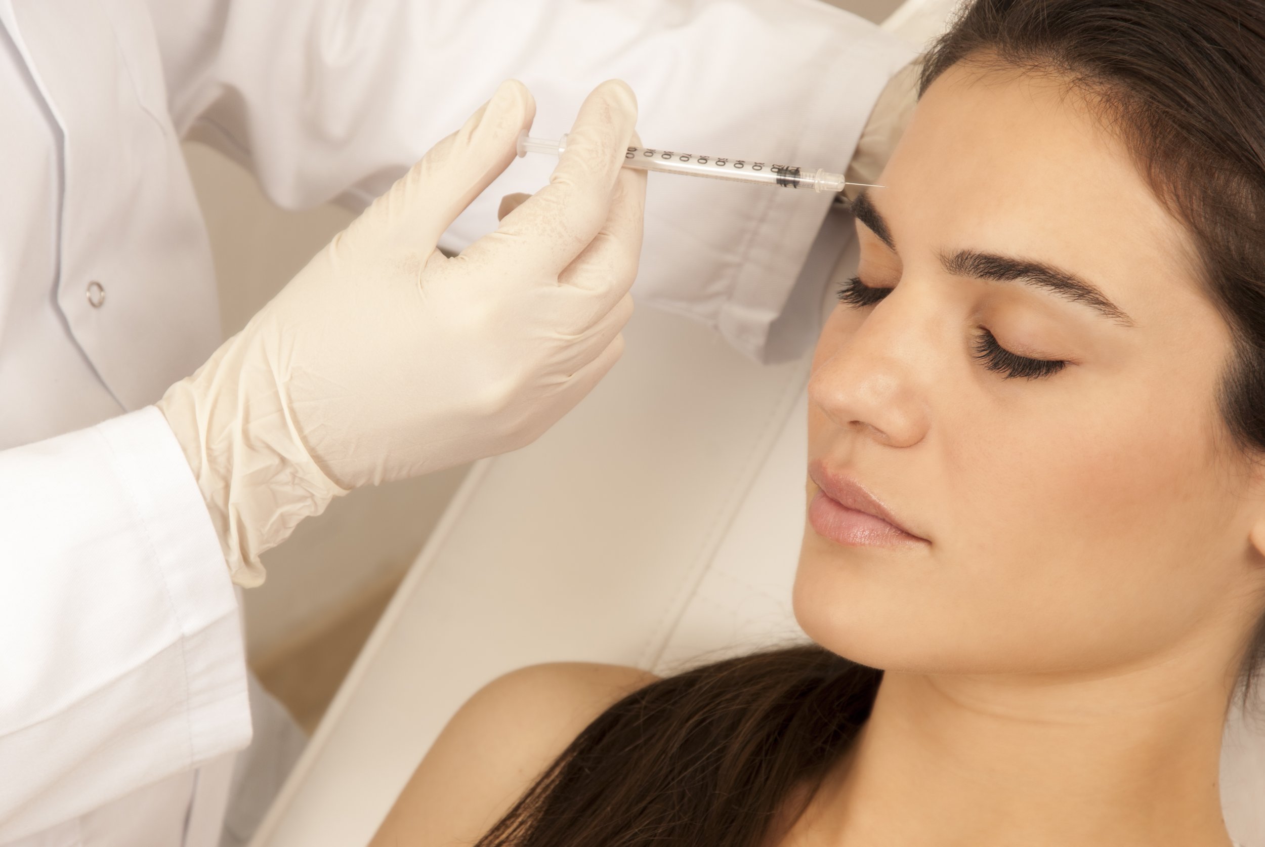 A healthcare worker in gloves administering an injection to a woman in a clinical setting.