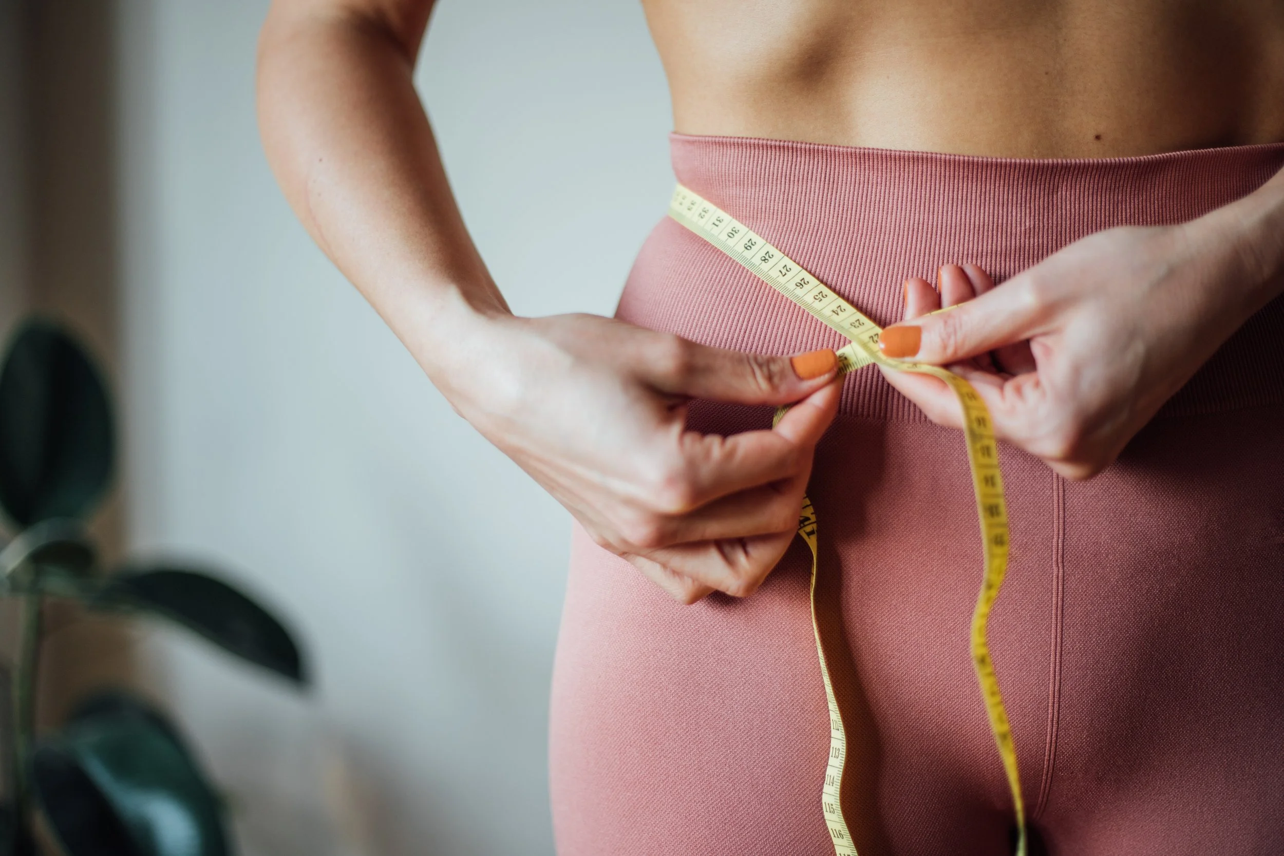 A person measuring their waist with a yellow tape measure while wearing pink workout leggings.