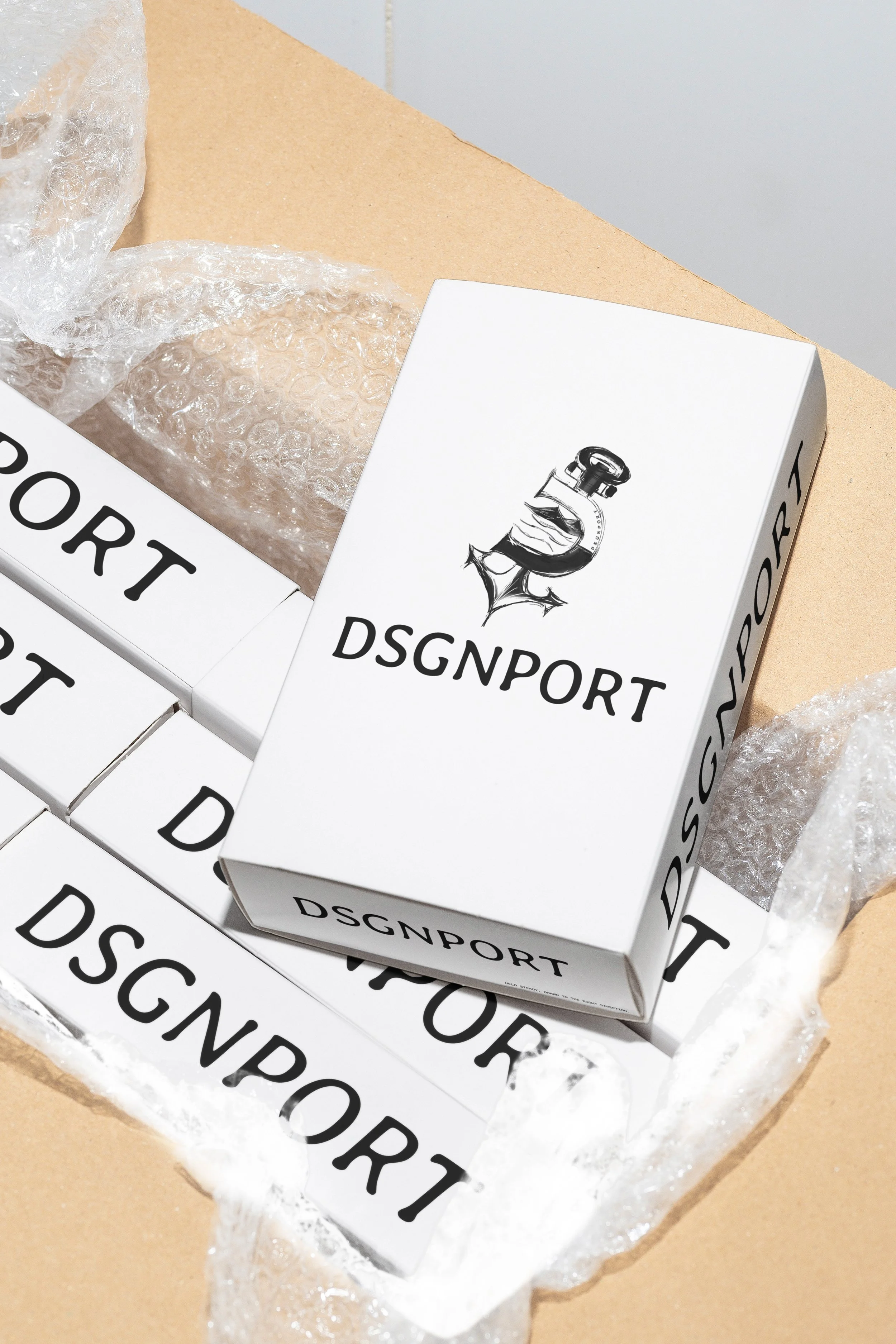Several white boxes with black text reading 'DSGNPORT' are stacked on a cardboard surface. Some of the boxes are partially covered with clear bubble wrap.