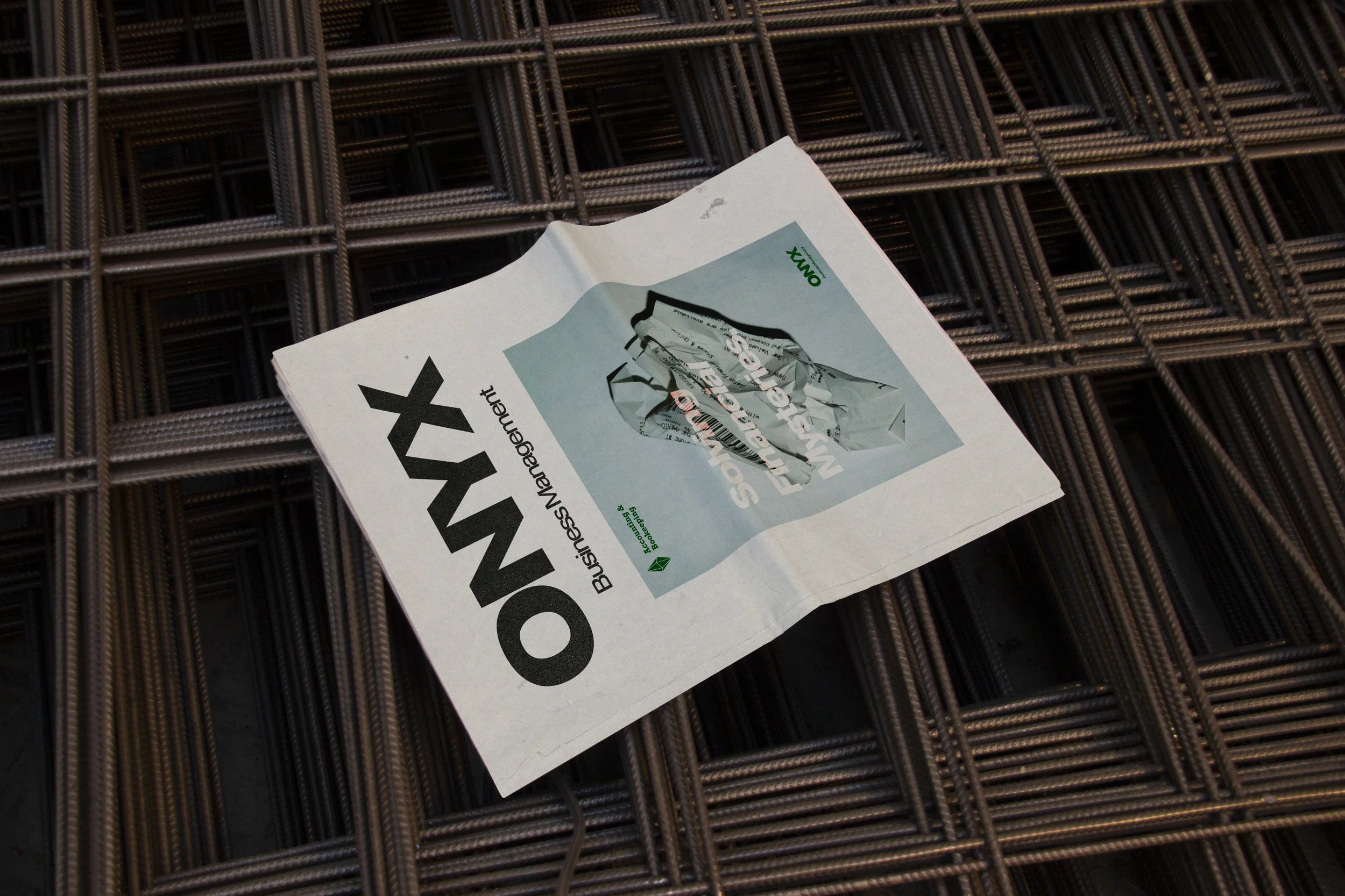 A business newspaper titled 'ONYX' resting on a stack of metal rebar.
