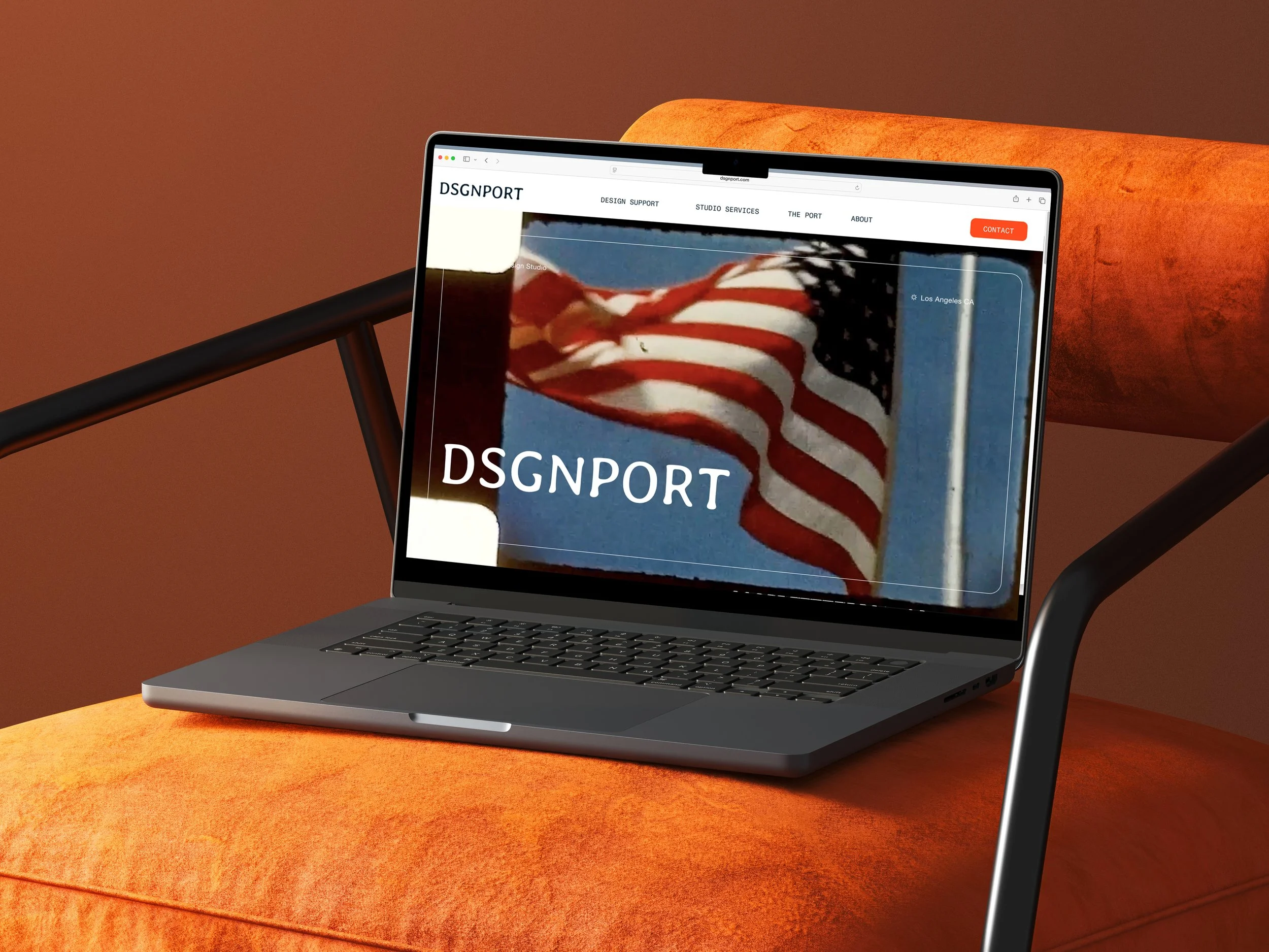 A MacBook laptop on a burnt orange lounge chair displaying a website with a large American flag and the text "DSGNPPORT".