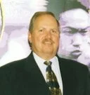 A man in a suit with a patterned tie standing in front of a large black-and-white portrait.