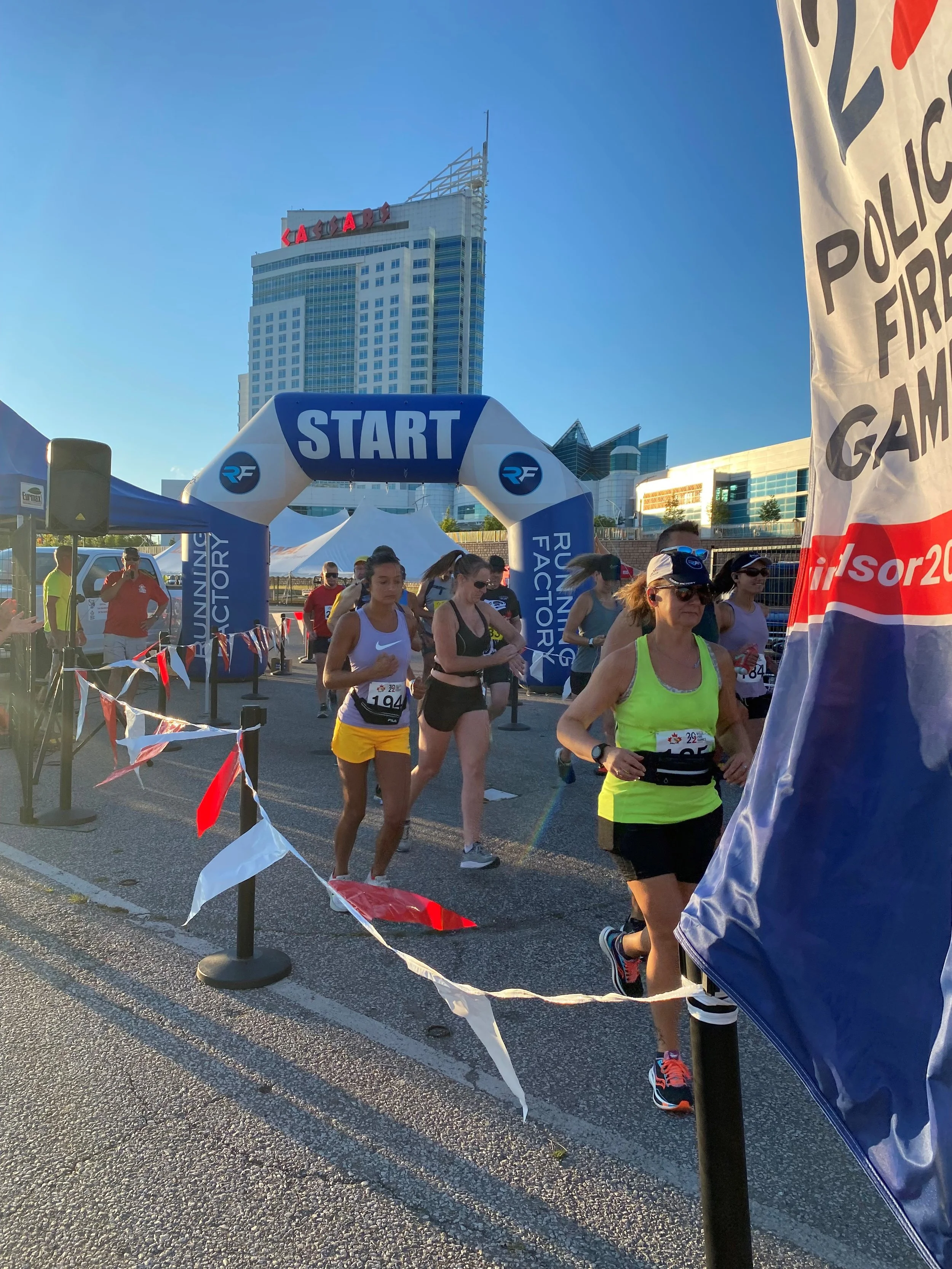 Runners starting a race at an outdoor event with an inflatable start line, tall buildings in the background, and a blue sky.