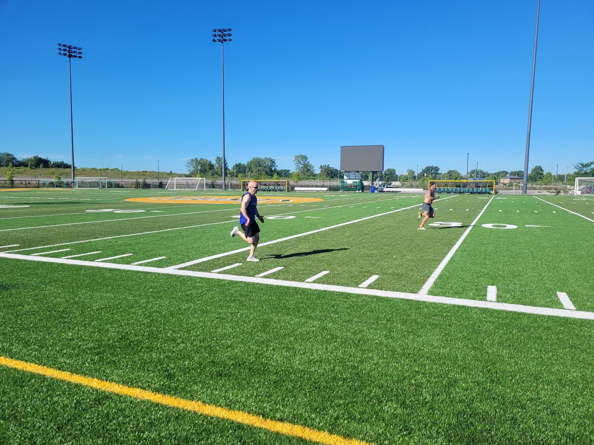 Two men running on a football field with bright blue sky overhead.