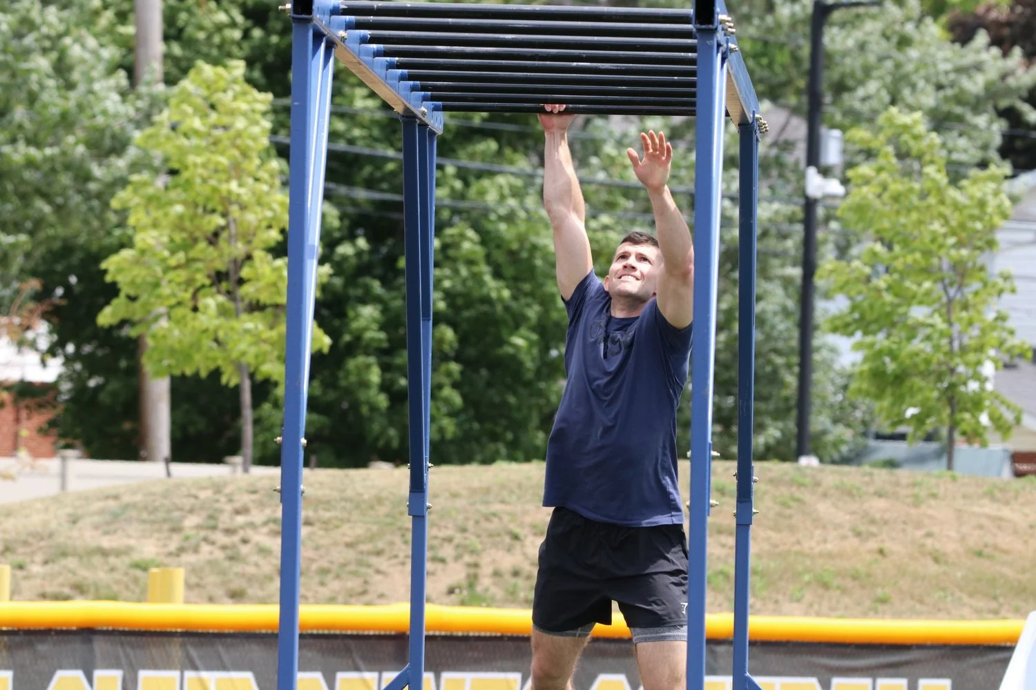Man in athletic clothing performing a pull-up on outdoor gym equipment during daytime.