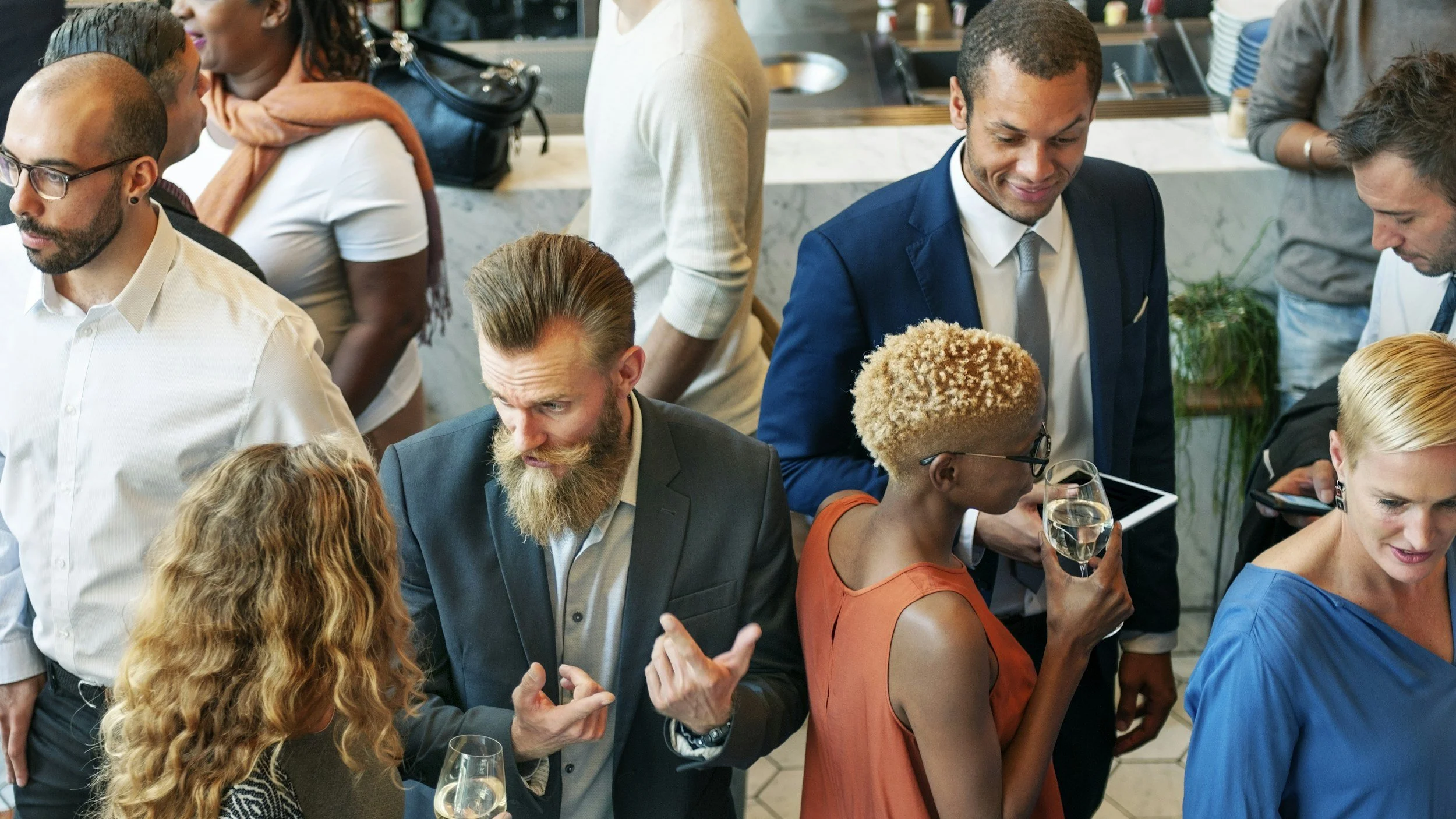 Group of people socializing at a restaurant or bar, holding drinks, and engaging in conversations. The setting appears lively and modern.