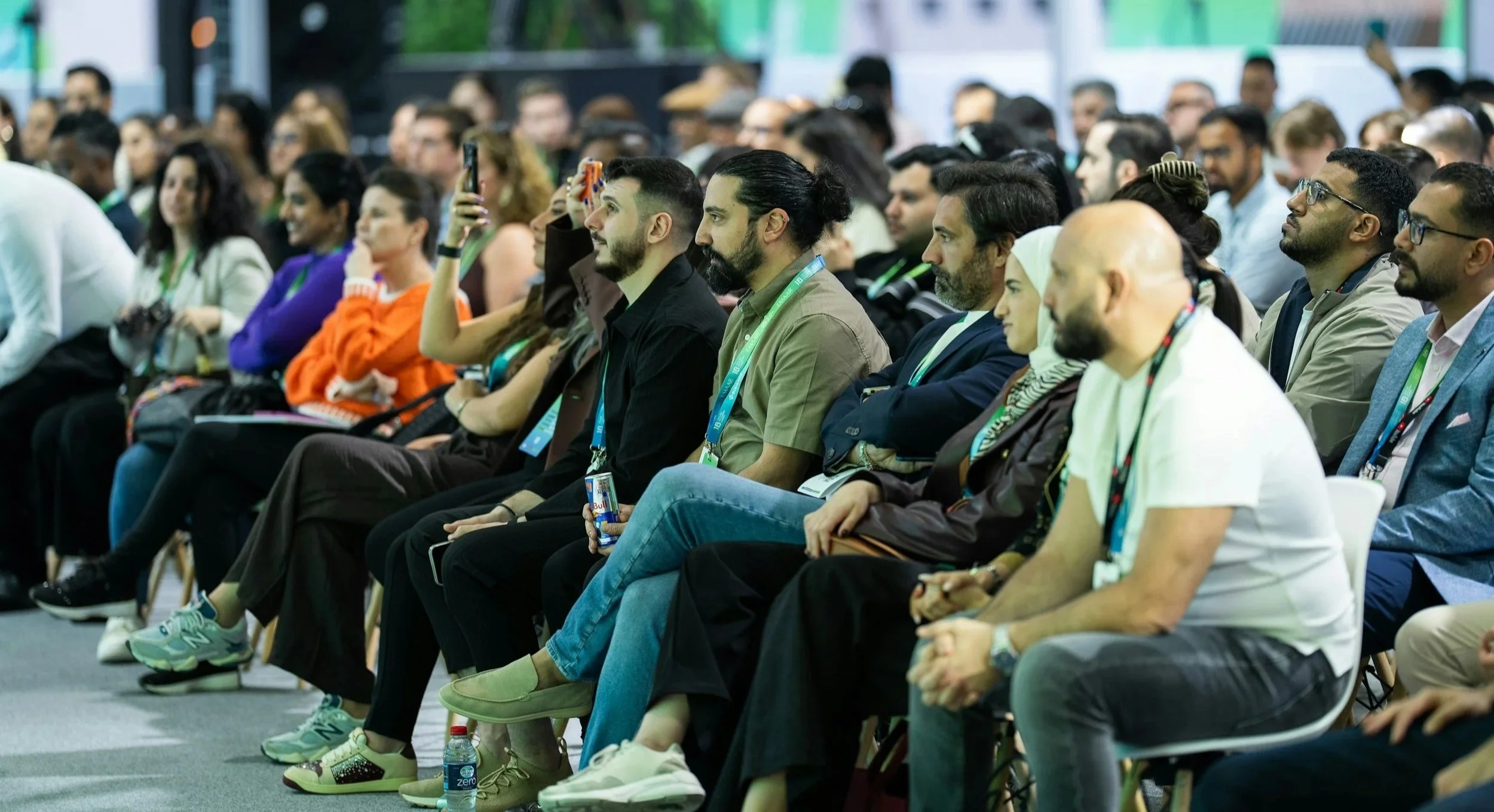 A large group of diverse people attending a conference or seminar, sitting in chairs and listening attentively.