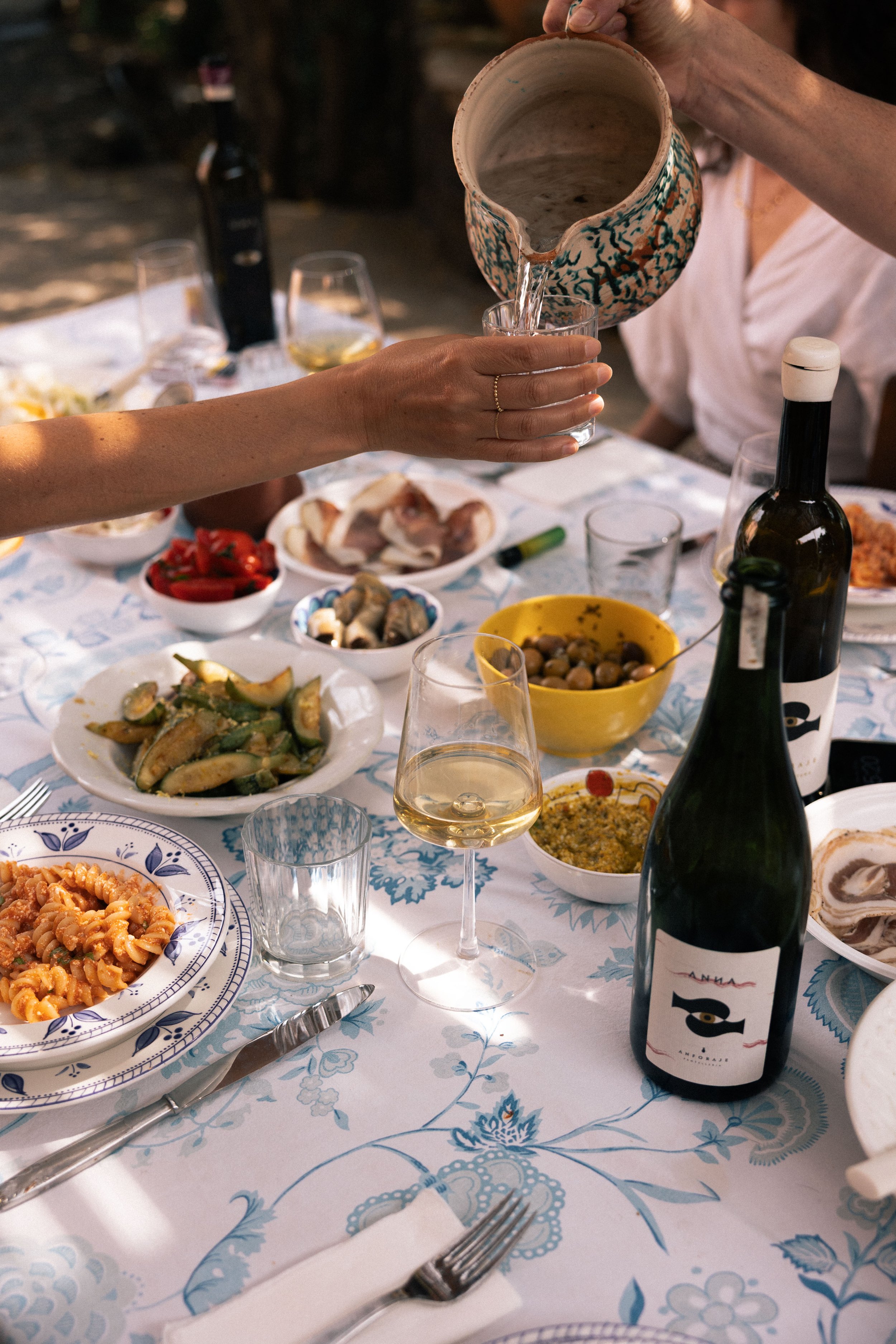 A summer table set for a meal with various dishes, with Anforaje wine bottles and glasses