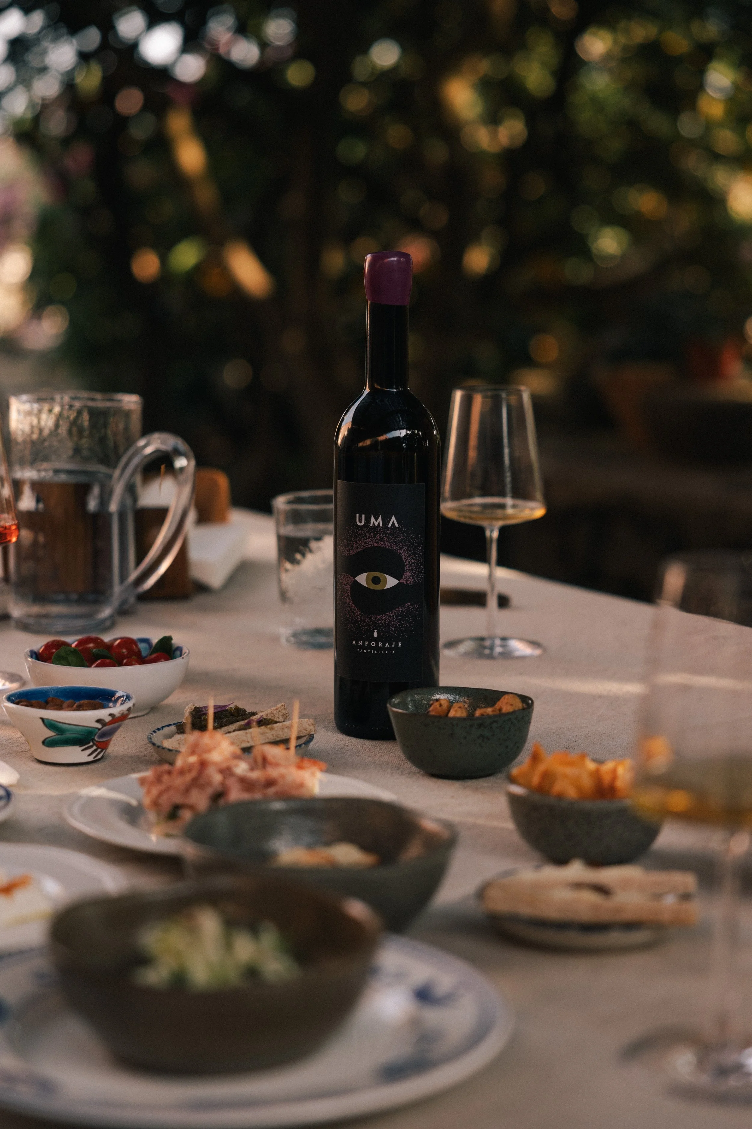 Anforaje Uma  wine bottle, and glasses set outdoors during a degustation evening.