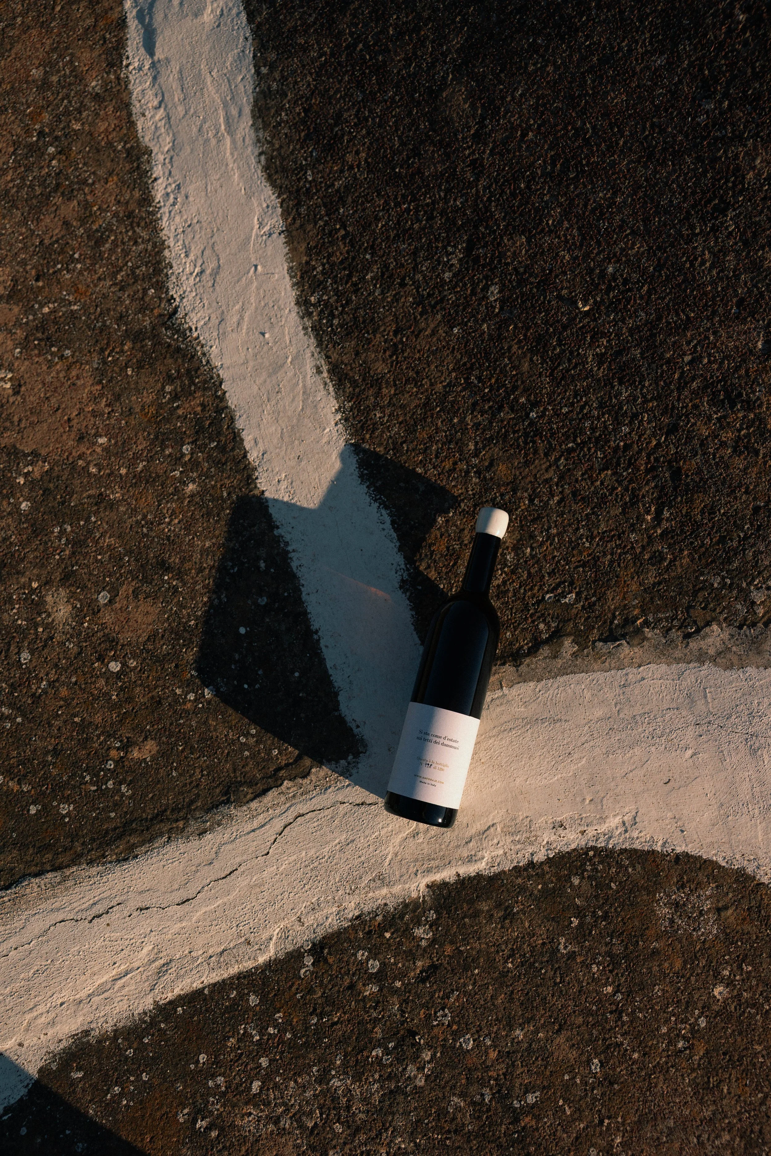 A bottle of Anforaje white wine on the roof of a dammuso in Pantelleria at sunset, casting its shadow.