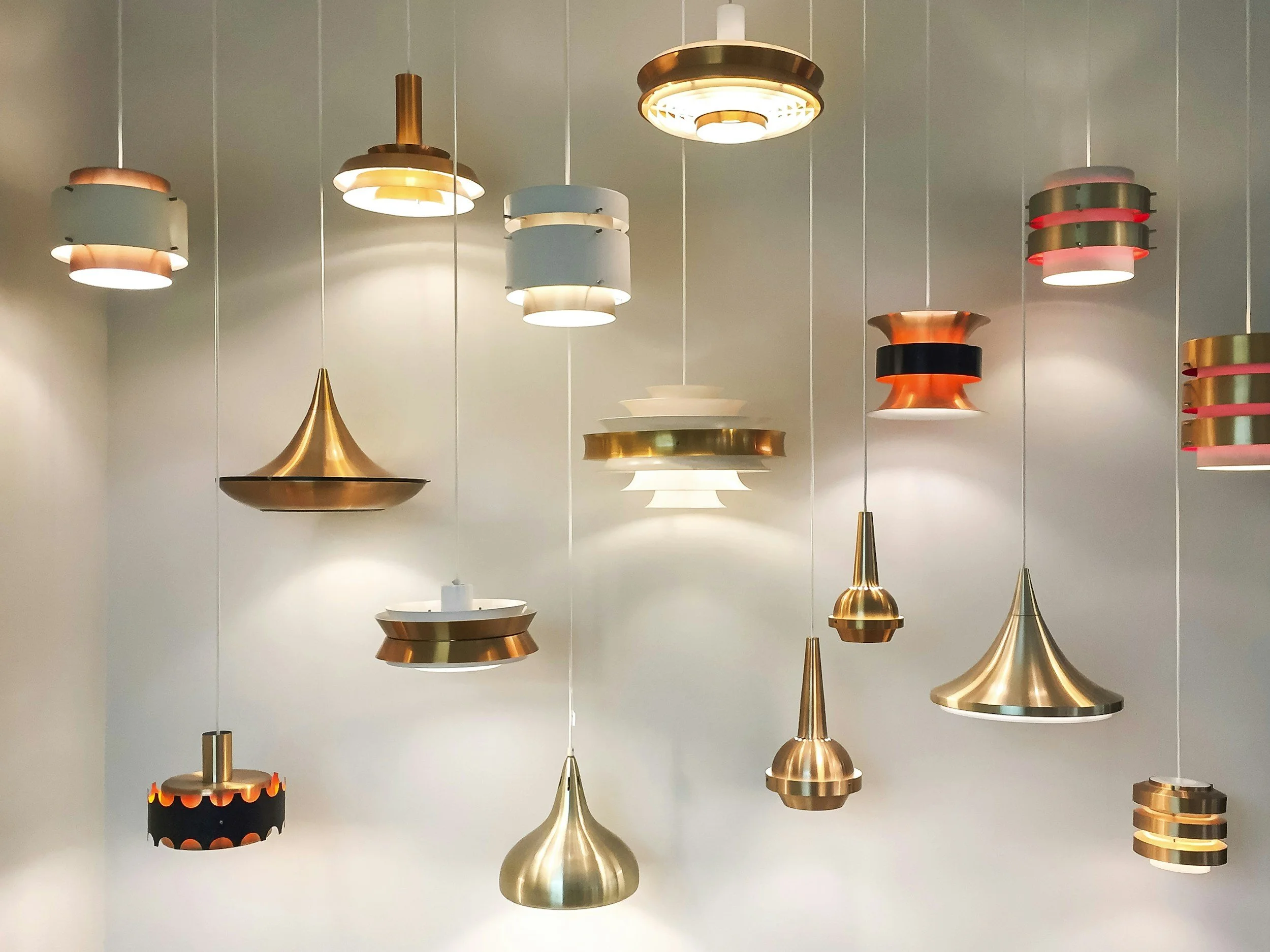 Various modern pendant ceiling lights in different shapes and metallic finishes, hanging in a showroom or display area.