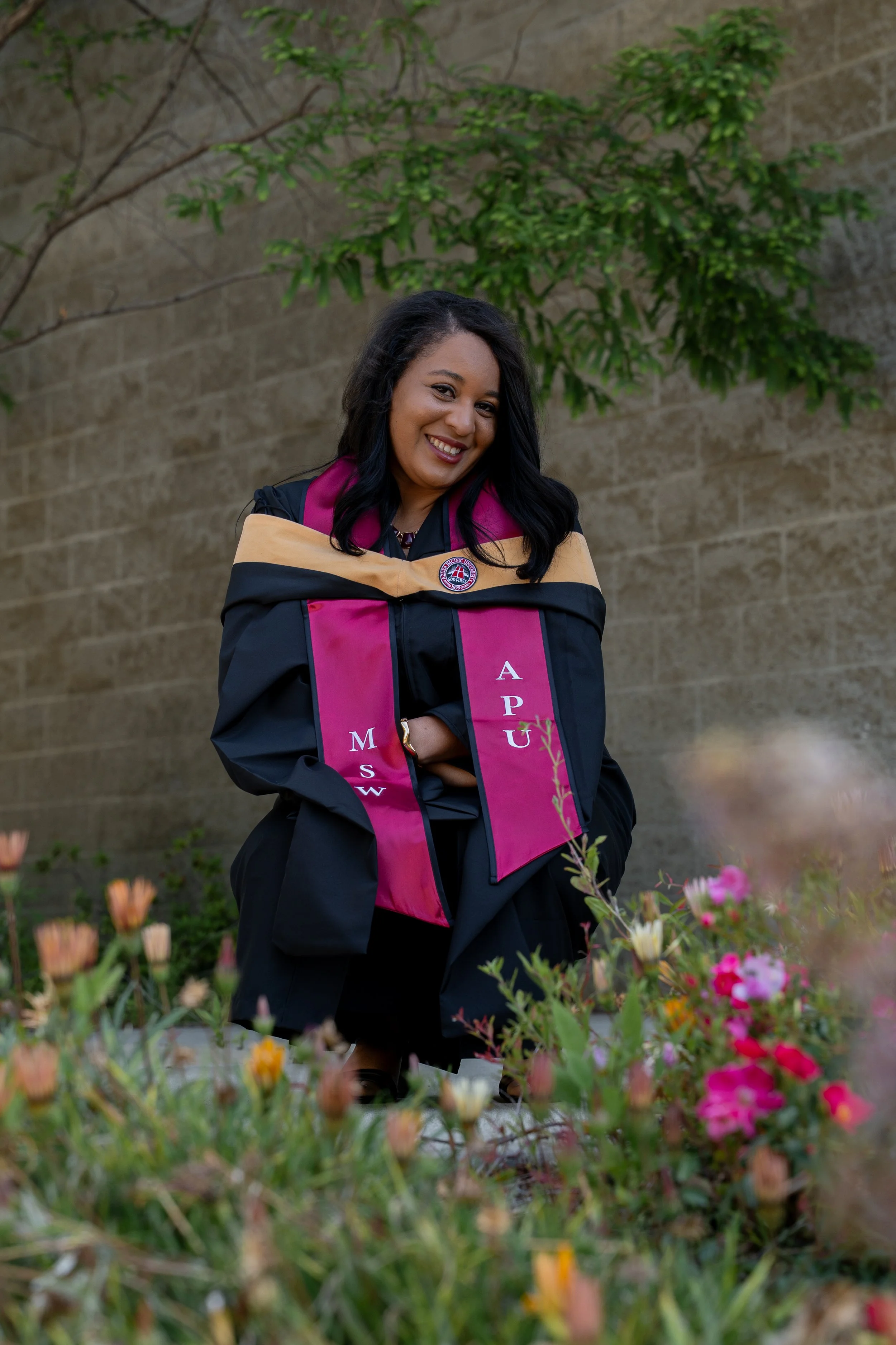 A woman in a graduation cap and gown standing in a garden with flowers.