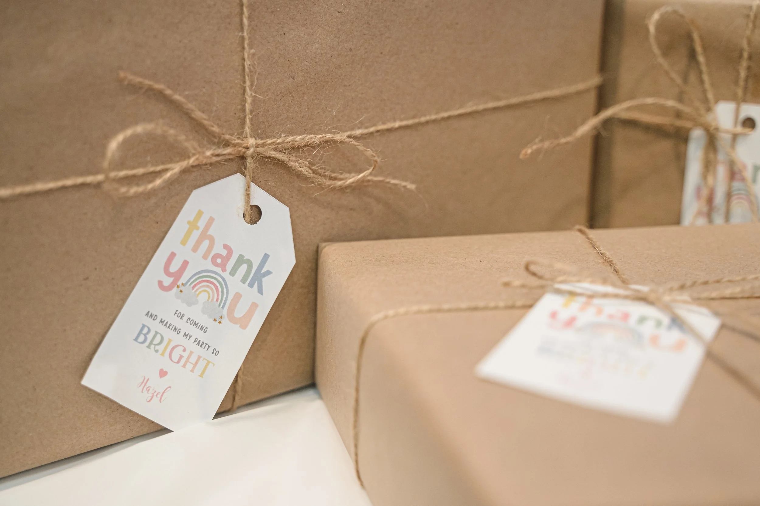 Close-up of a cardboard gift box wrapped with twine and a colorful thank you tag attached, with another box partially visible.