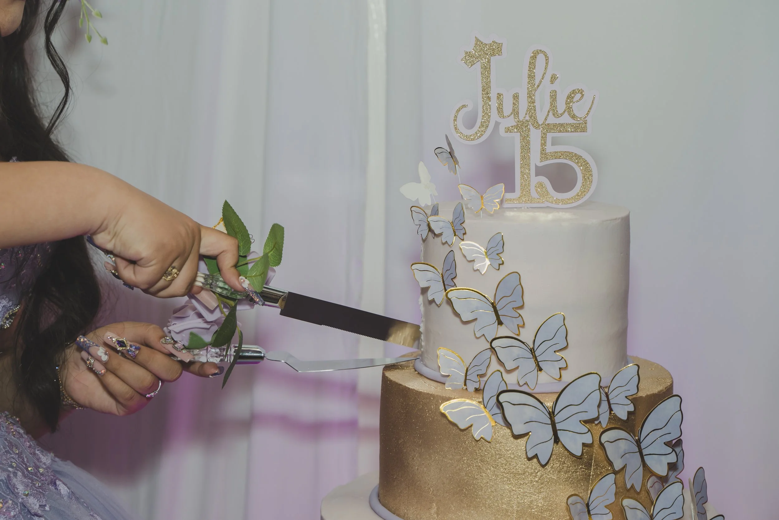 Woman decorating a white birthday cake with butterfly decorations and a 'Julie 15' cake topper.