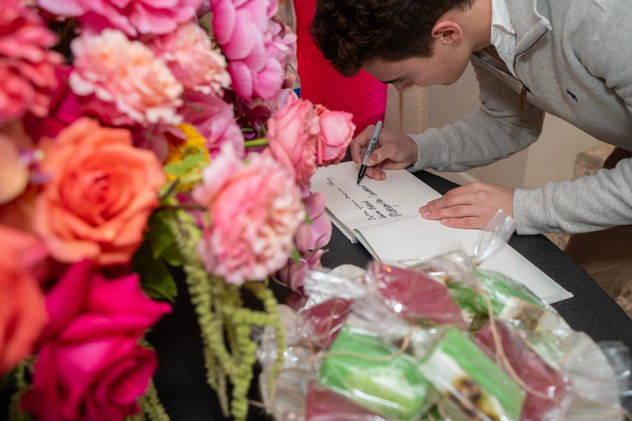 Young man signing a guest book at a floral arrangement event.