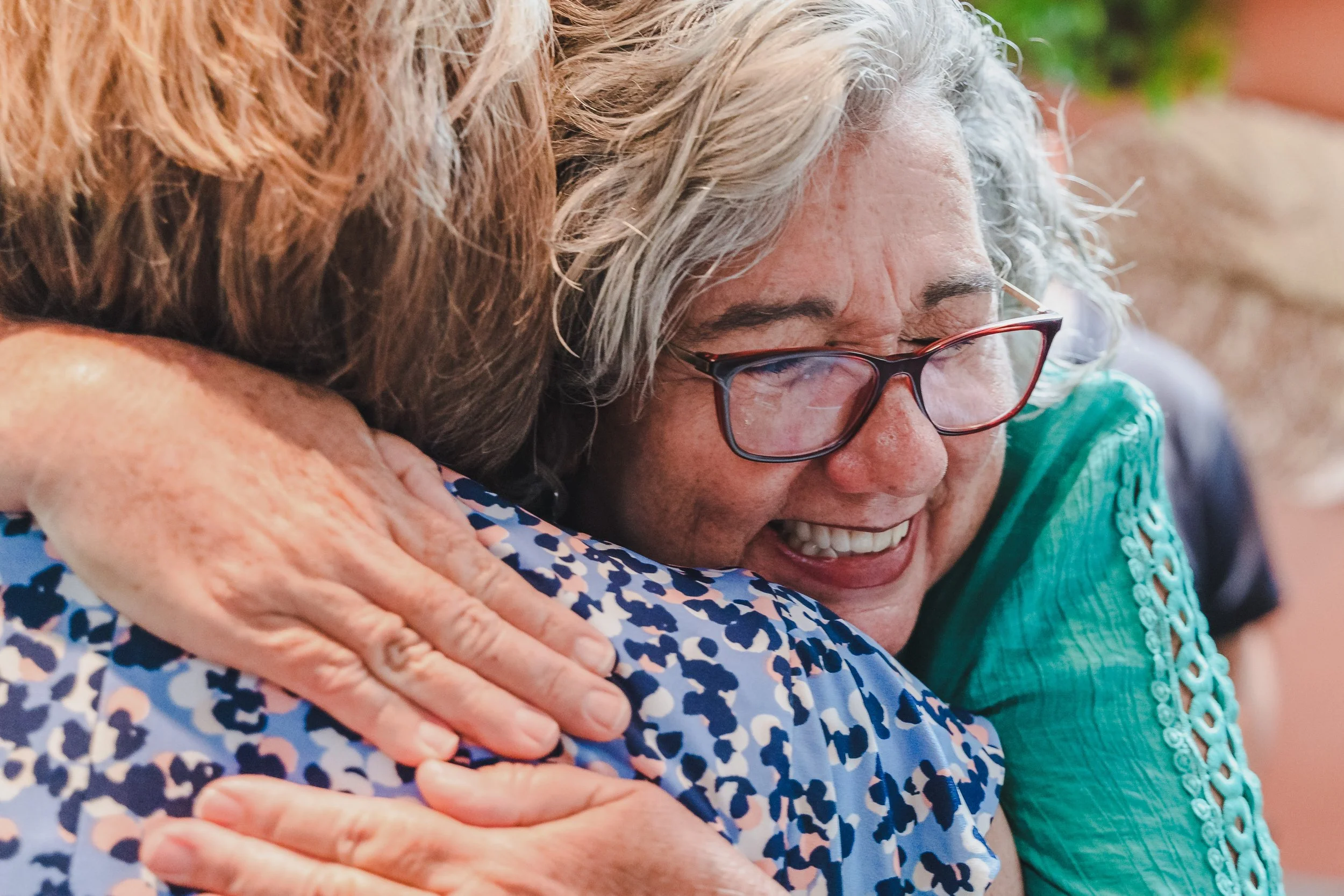 Two women hugging each other warmly, smiling and showing affection.
