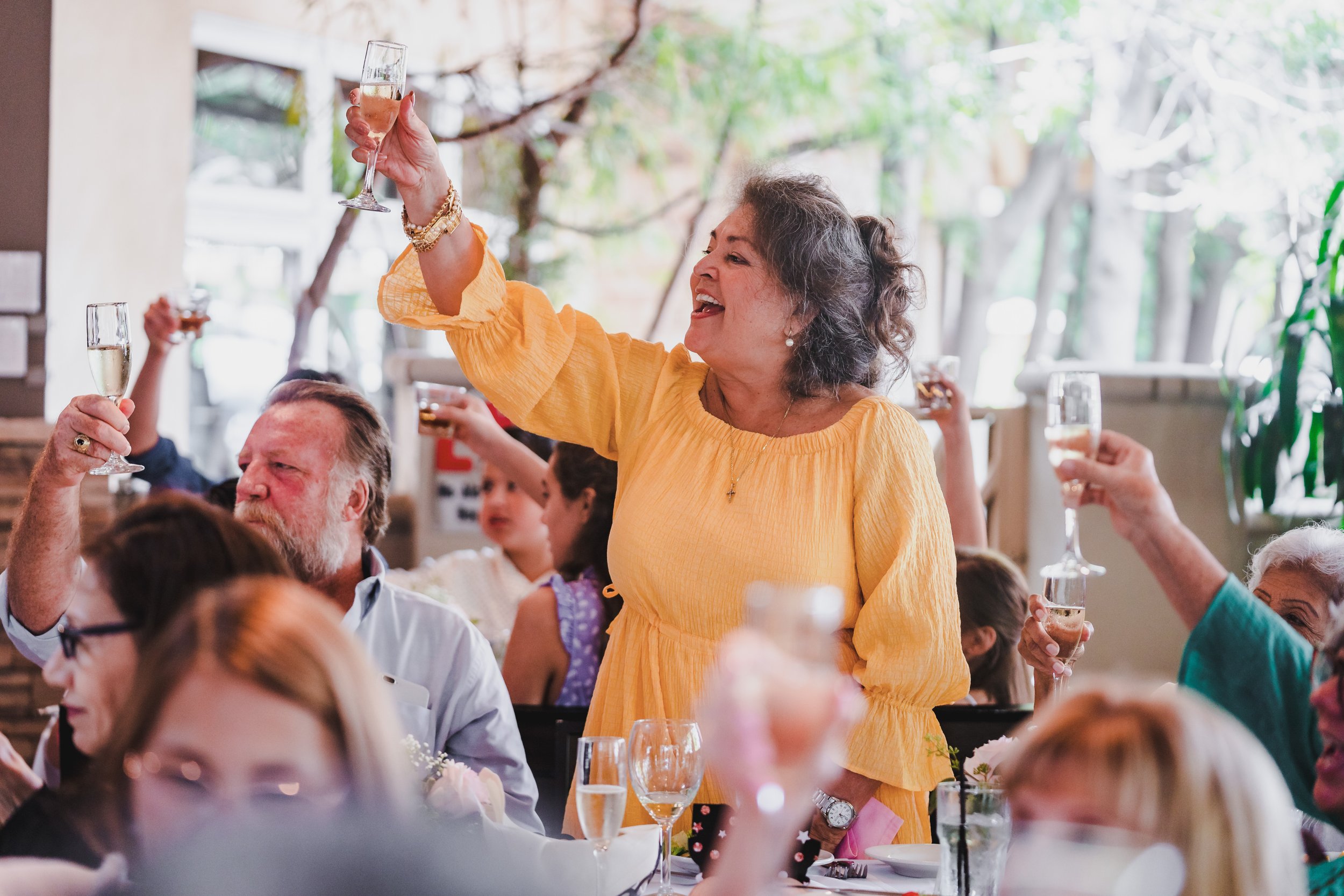 A woman in a yellow dress raising a glass of champagne during a celebration at a dinner party.