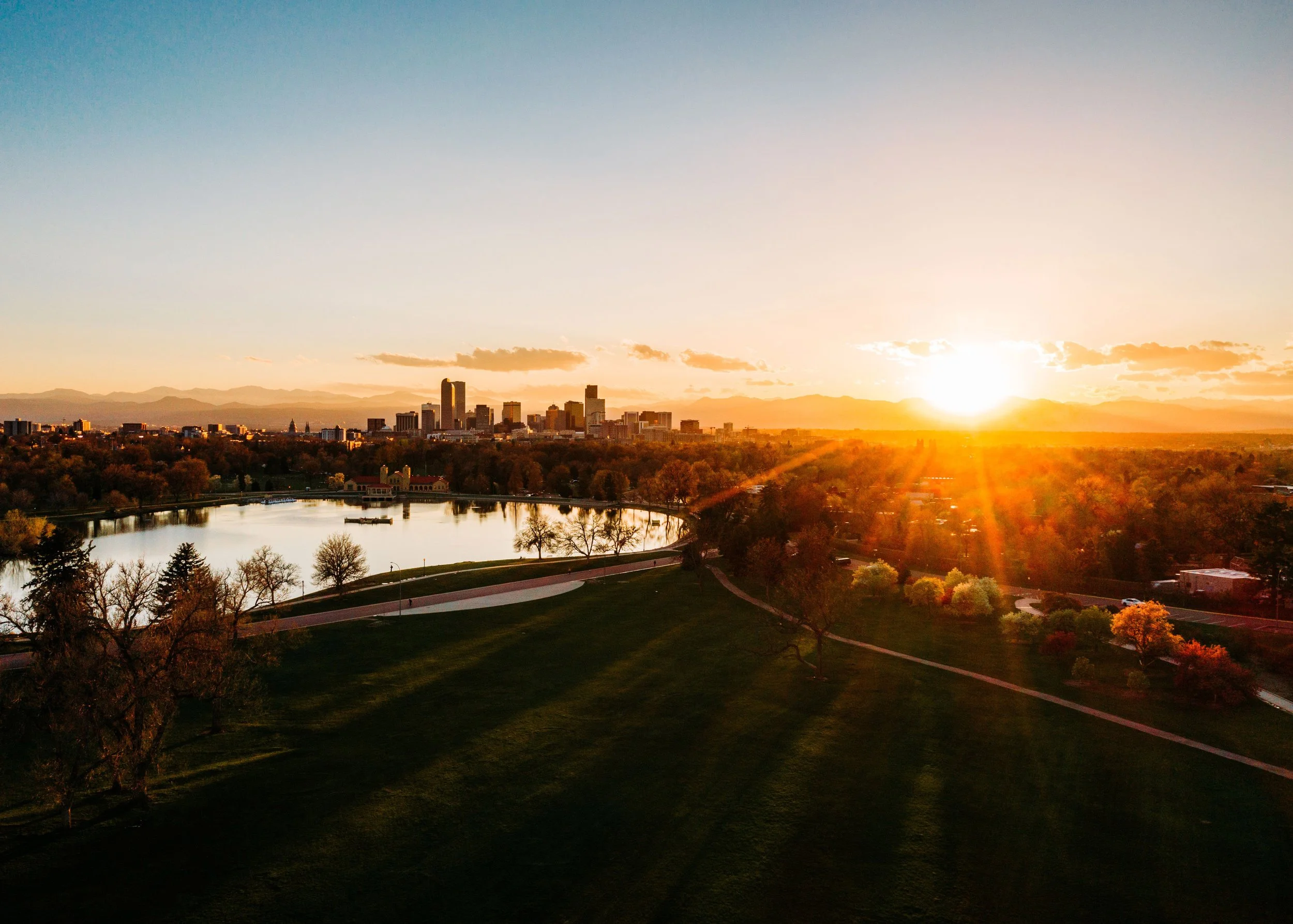 Aerial view of Denver, Colorado skyline at sunset with City Park lake and Rocky Mountains in the background