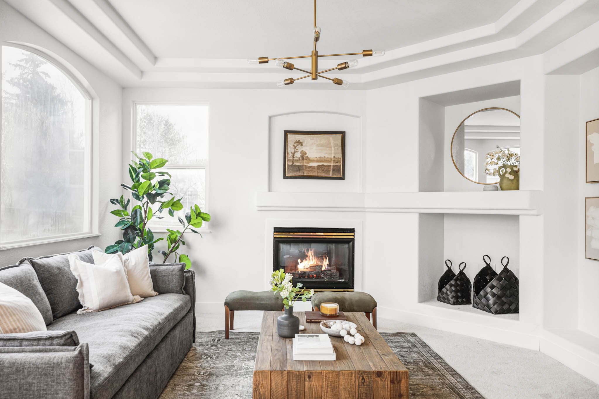 Renovated living room at 10499 Cheetah Winds in Lone Tree Colorado, featuring a gas fireplace with arched surround, tray ceiling with brass chandelier, and built-in niche detail by The Rukavina Companies