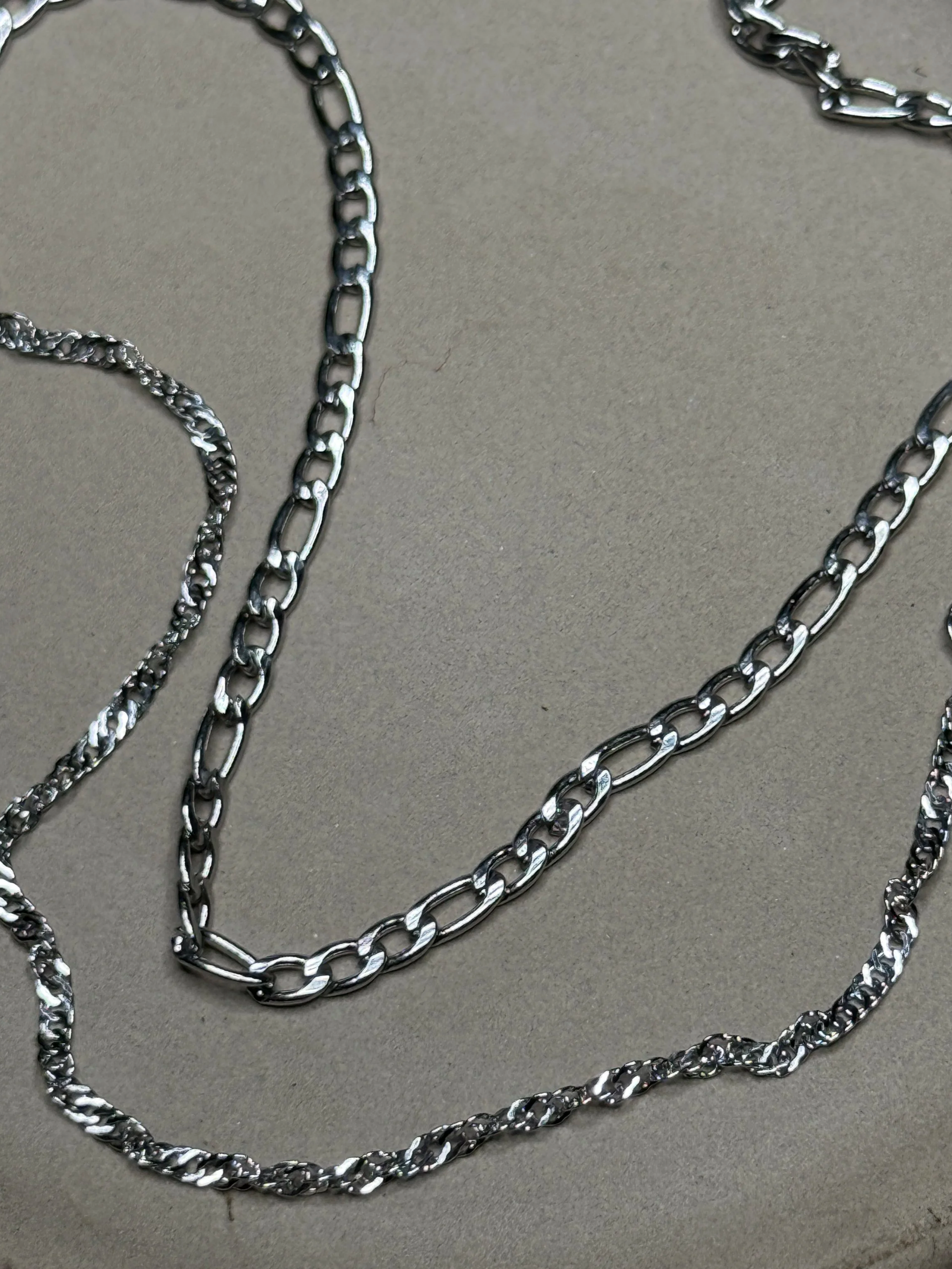 Multiple silver necklaces with different chain styles laid out on a gray surface.