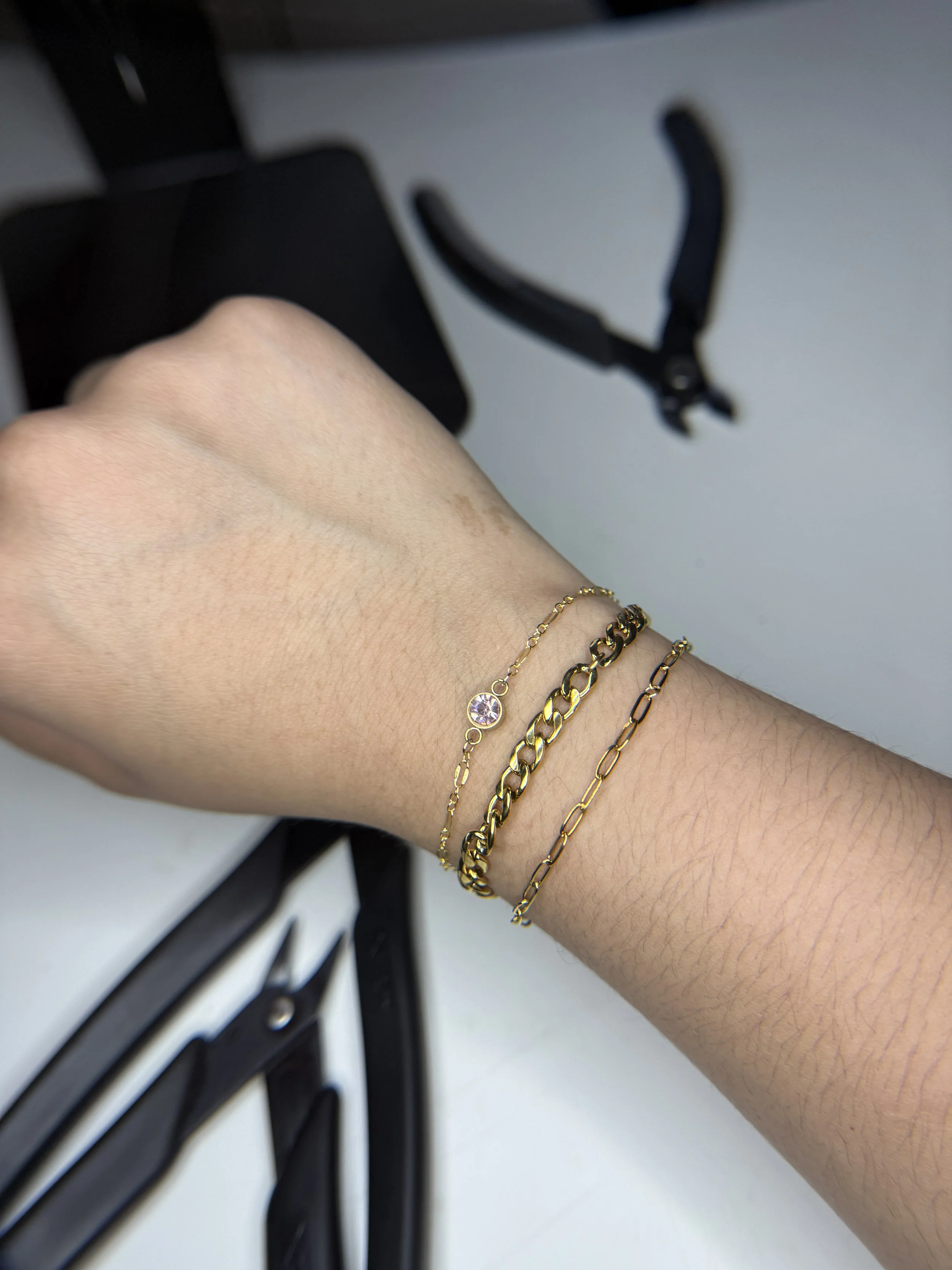 A person's arm with gold bracelets, held in front of a white surface and black metal object.