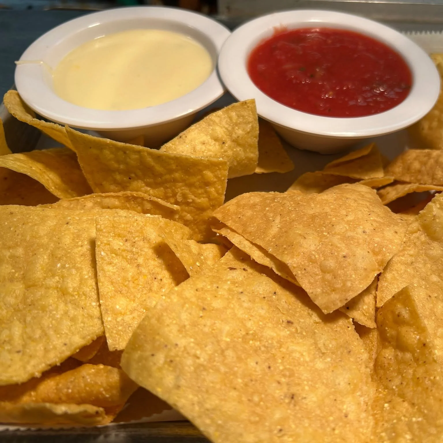 Tortilla chips with two bowls of salsa and cheese sauce.