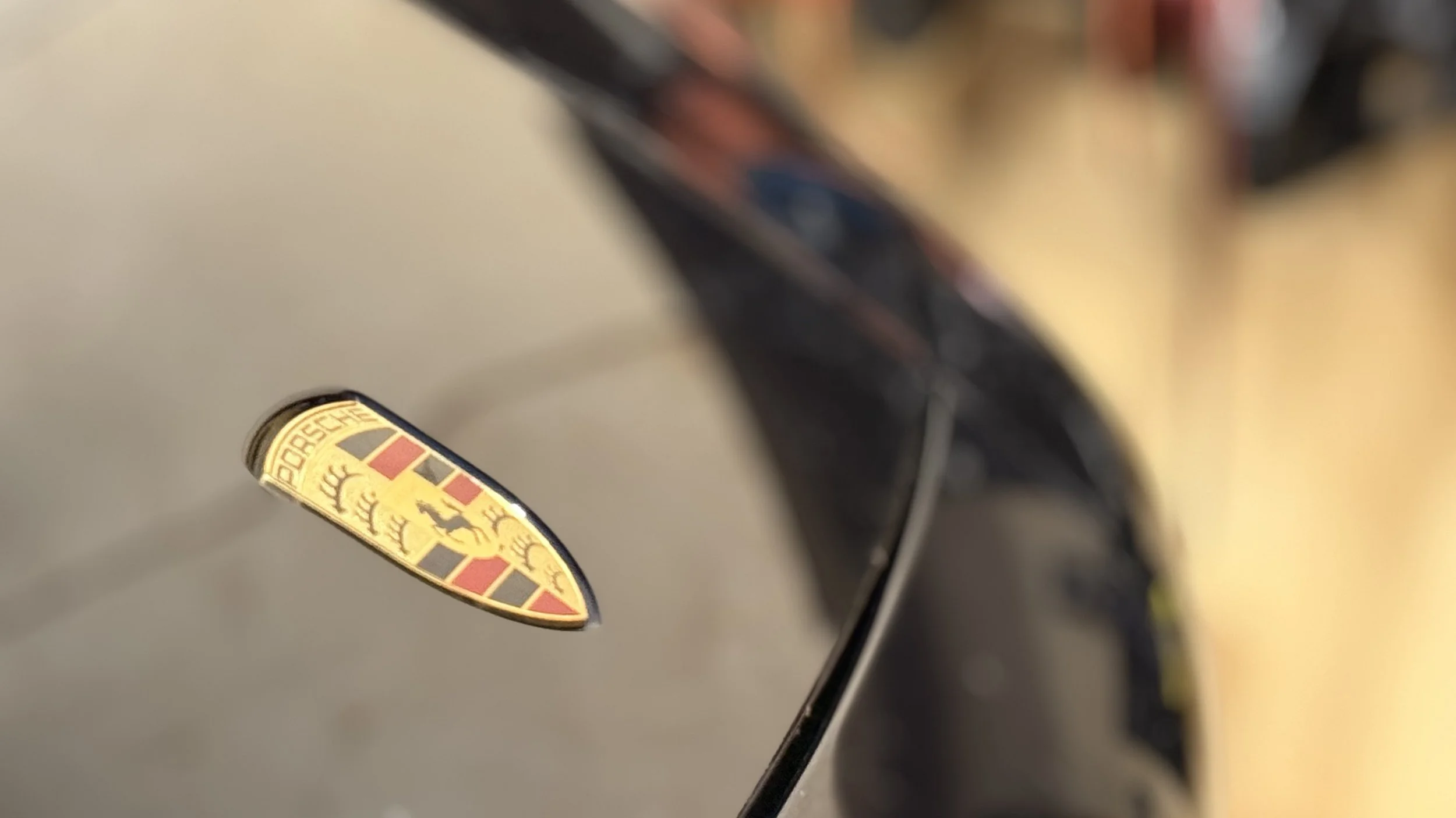 Close-up of a Porsche emblem on a car's hood, showing a crest with a horse and the word 'Porsche'.