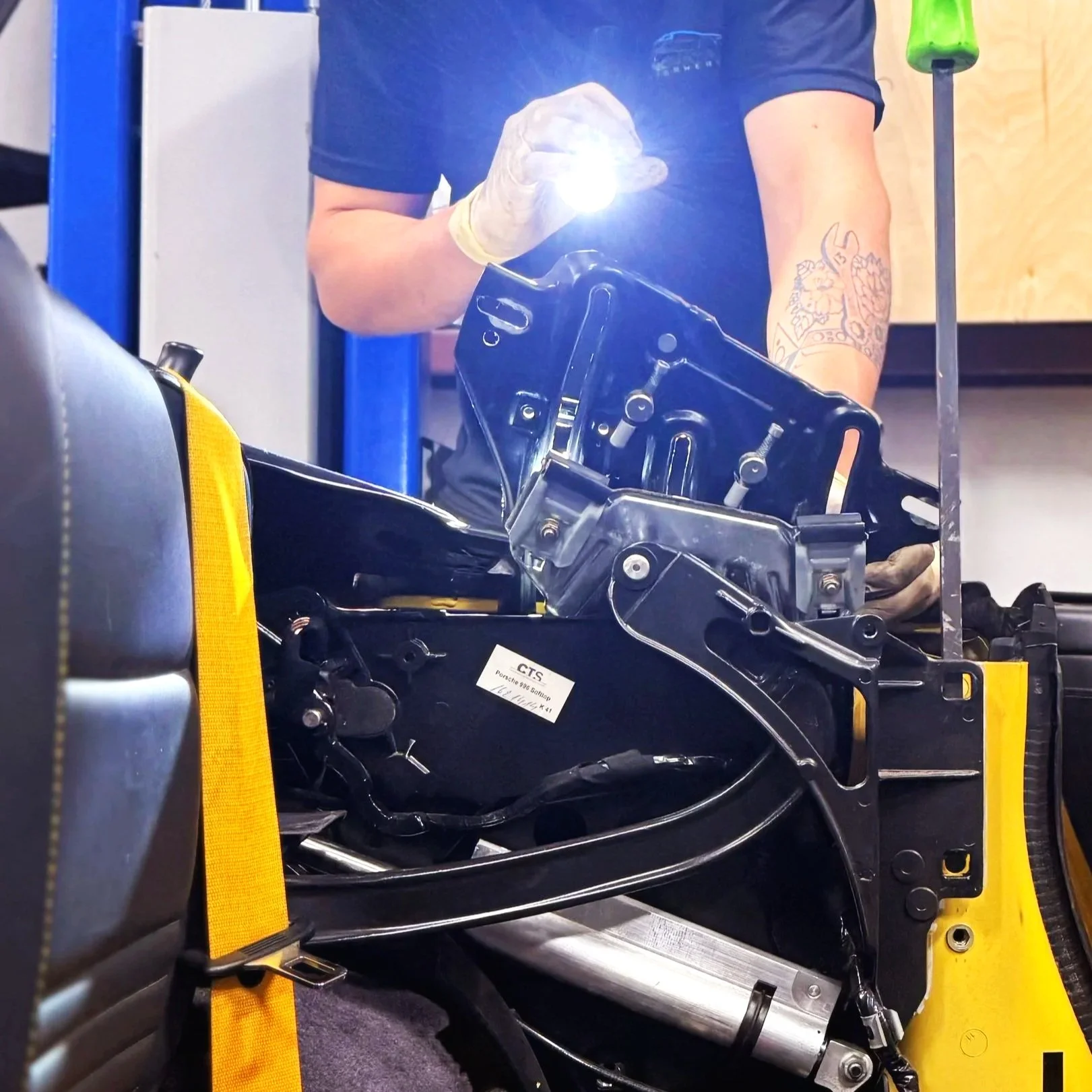 Person working on a motorcycle frame, wearing gloves, in an indoor workshop.