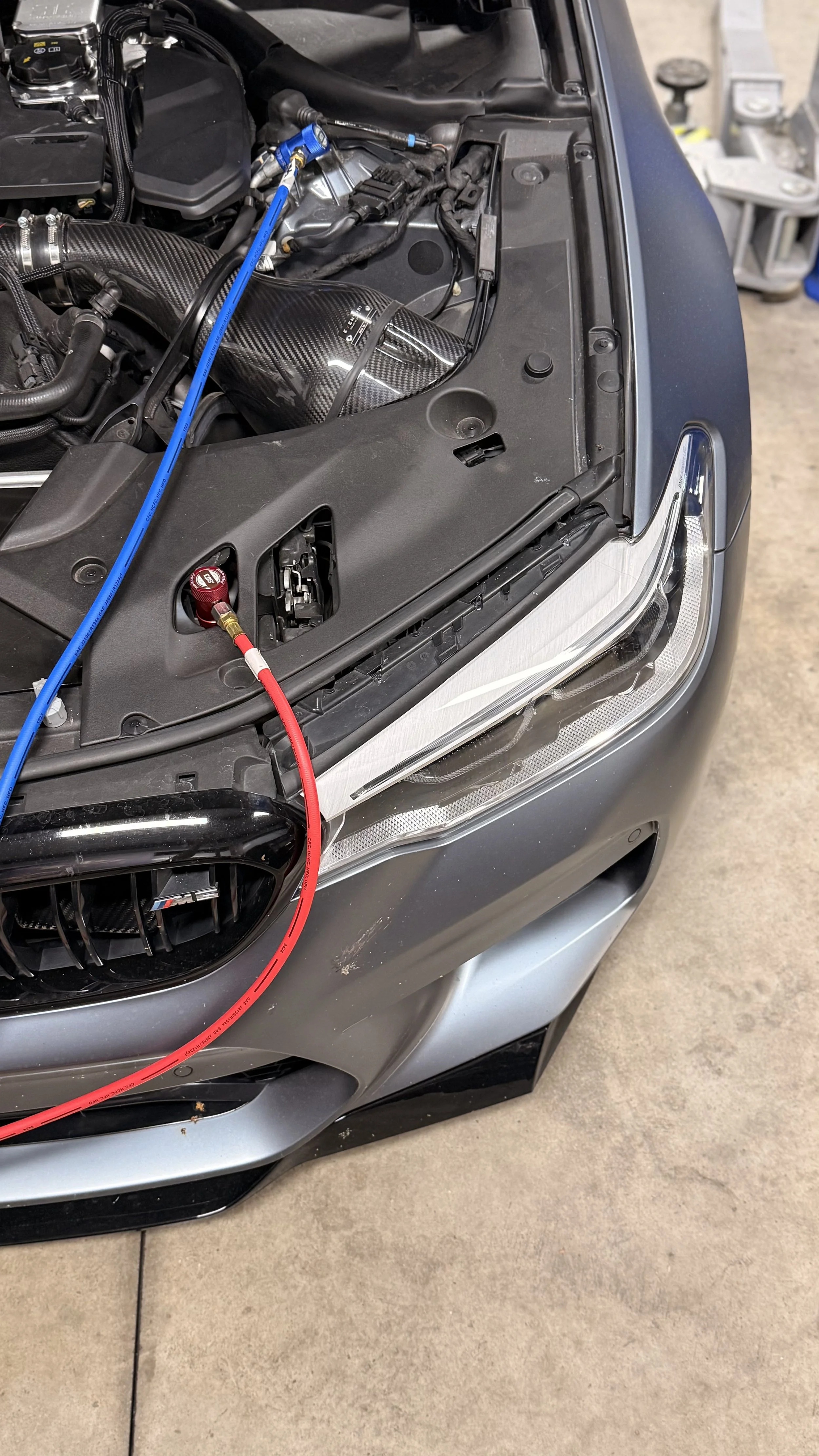 Close-up of a car engine bay showing a carbon fiber air intake and red and blue testing equipment connected to the engine.