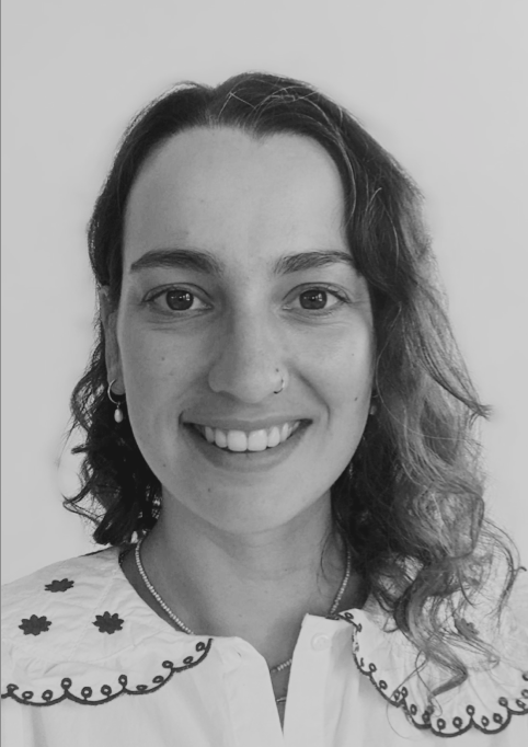 Black and white photo of a woman smiling, with wavy hair and nose piercing, wearing a embroidered blouse.