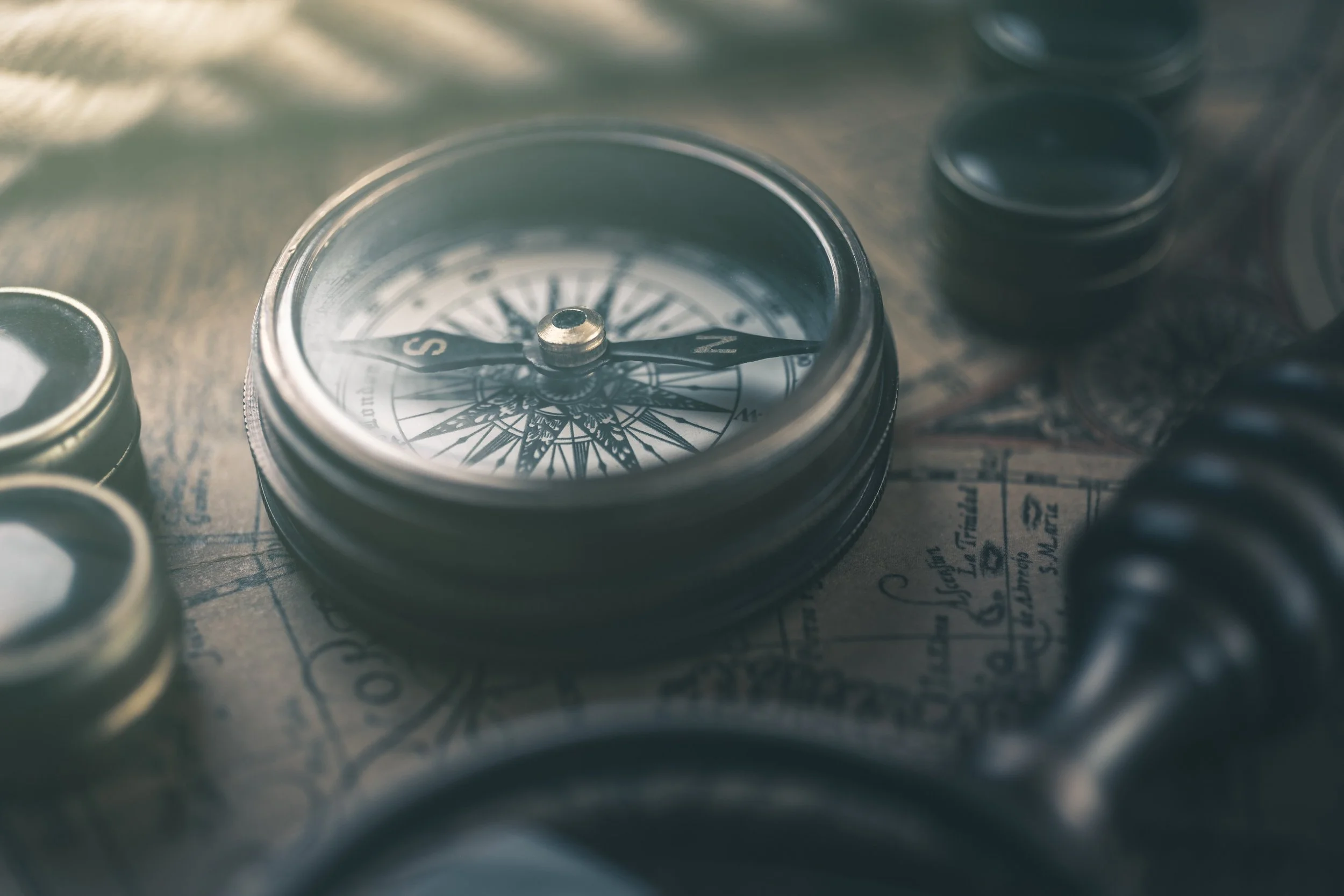 Close-up view of a vintage compass on top of an old map, with other compass containers nearby.