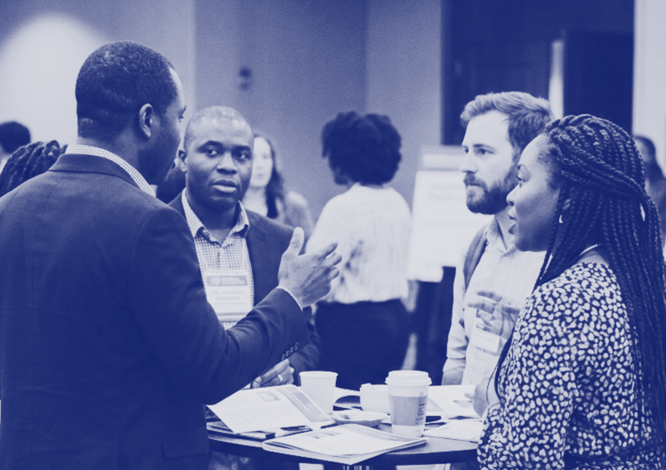 A group of mental health professionals having a discussion at a conference or event, some taking notes, with coffee cups and papers on table.