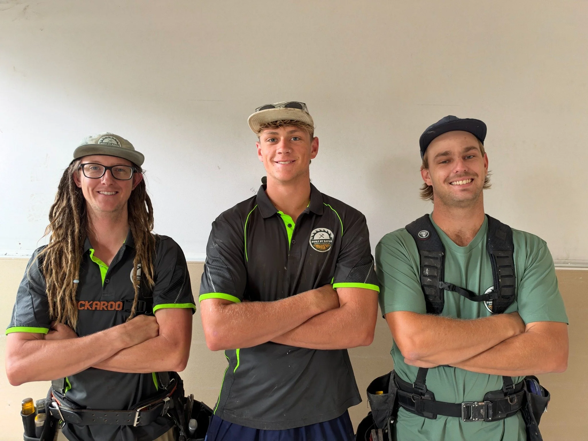The three-person Built By Bayer building team standing together on site in work clothes and tool belts.