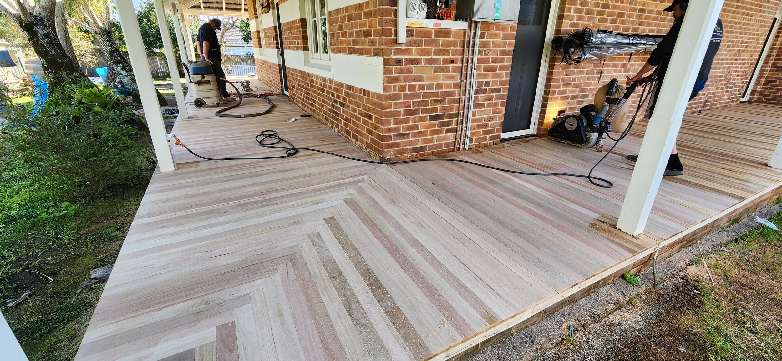 Workers installing a tile or wood flooring on a porch attached to a brick house