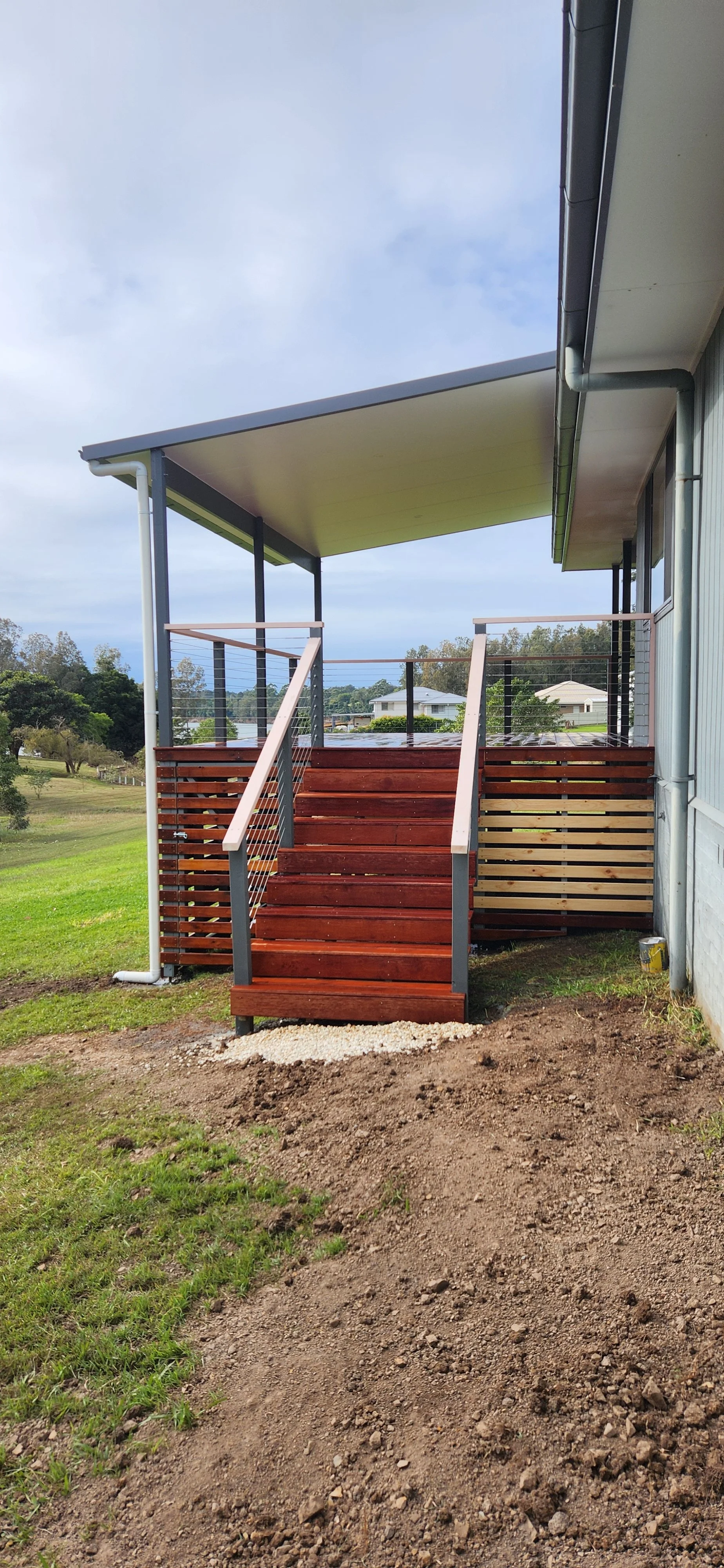 Wooden stairs leading to a backyard porch of a modern house with landscaped yard and neighboring houses in the background.