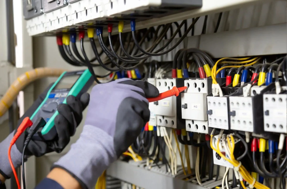 Technician testing electrical panels with a multimeter.