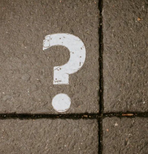 White painted question mark on brown tiled sidewalk.