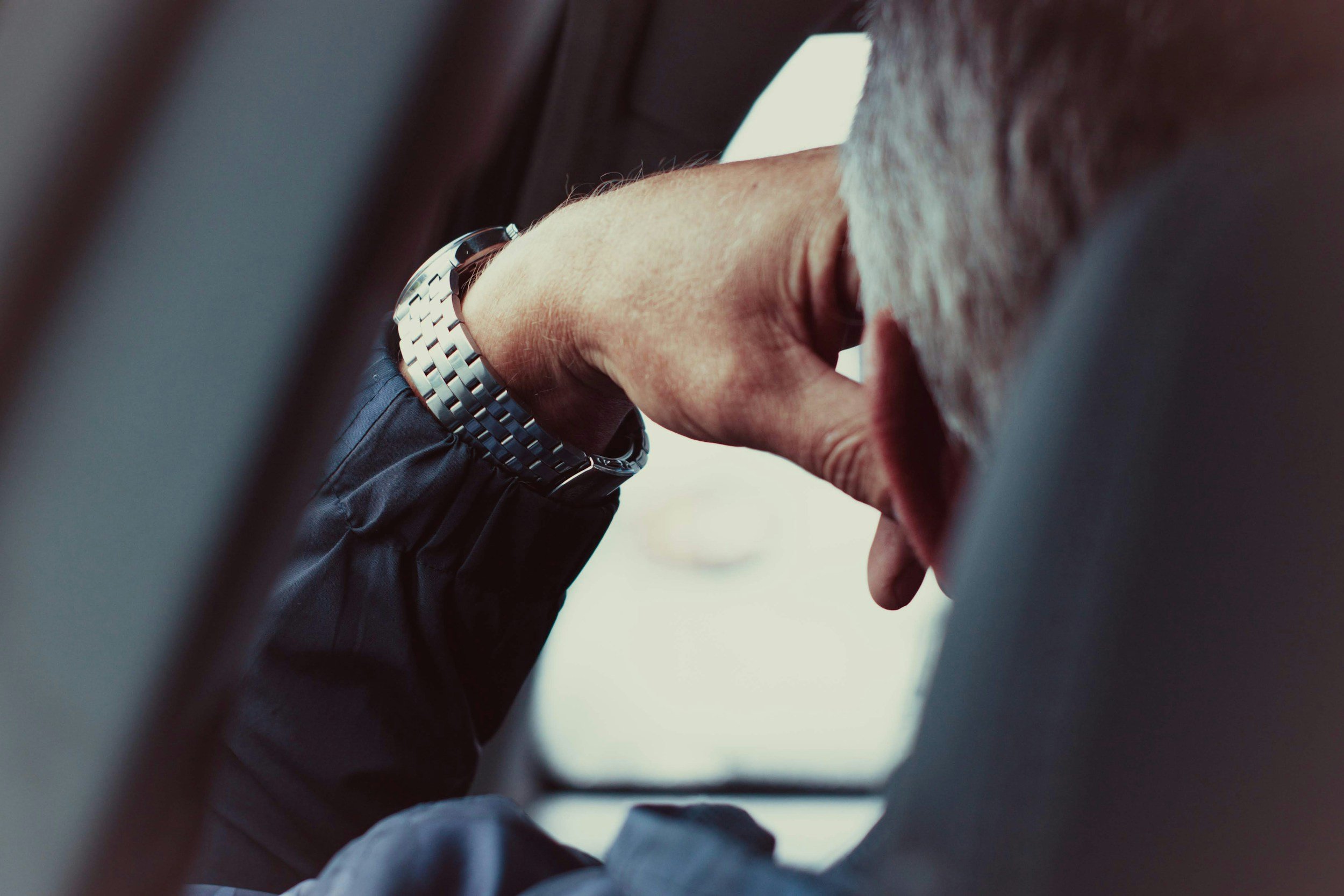 Close-up of a person's arm with a wristwatch, reaching out to touch or hold the hand of another person with lighter skin, in an indoor setting.